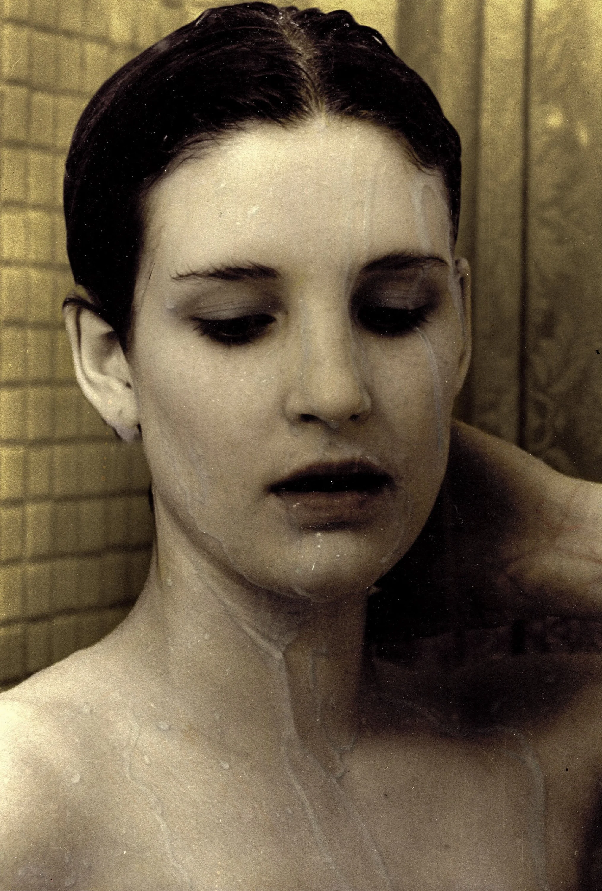 Close-up of a woman with wet hair, closed eyes, and water on her face and shoulders, against a gold gradient background.