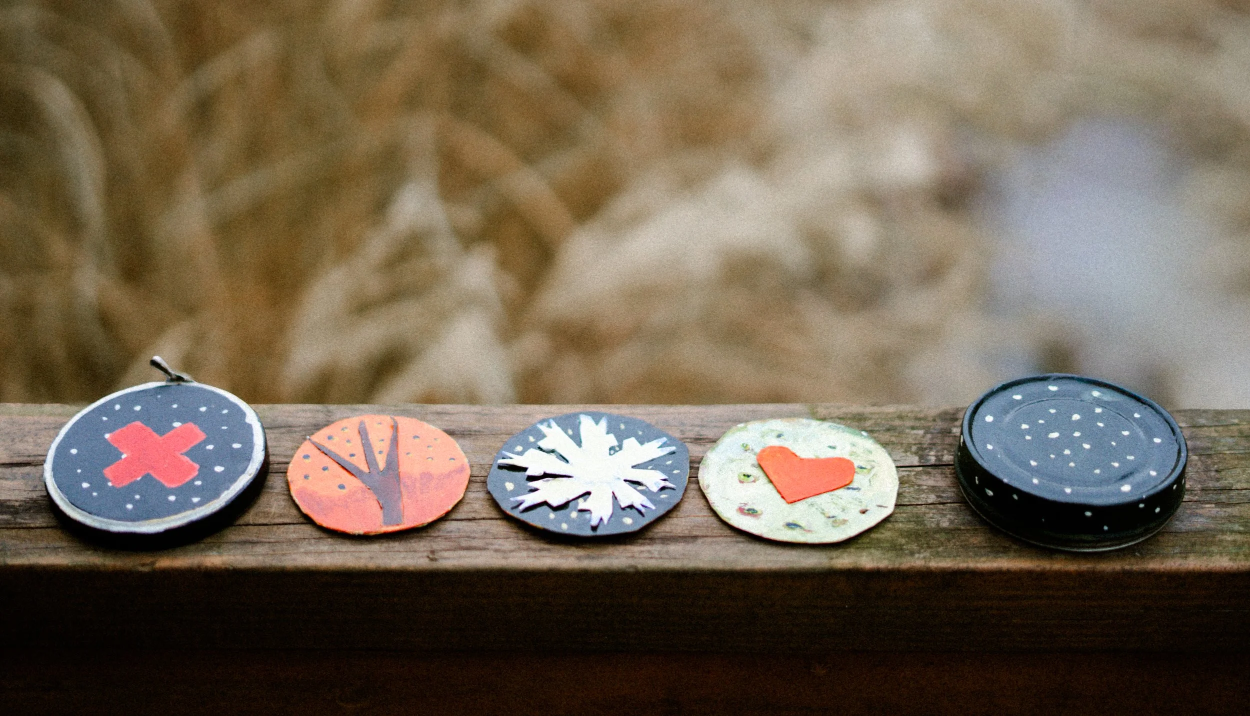 Colorful circular pins with various designs, including a red X, a tree, a snowflake, a heart, and a polka-dotted pattern, laid out on a wooden surface.