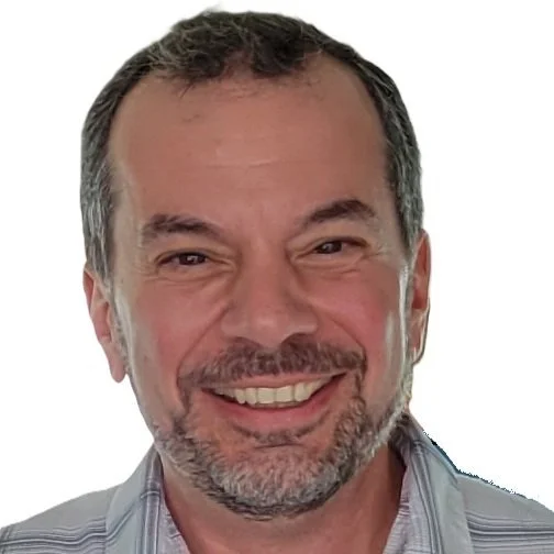 Close-up of a smiling middle-aged man with short dark hair, a beard, and mustache, wearing a collared shirt.