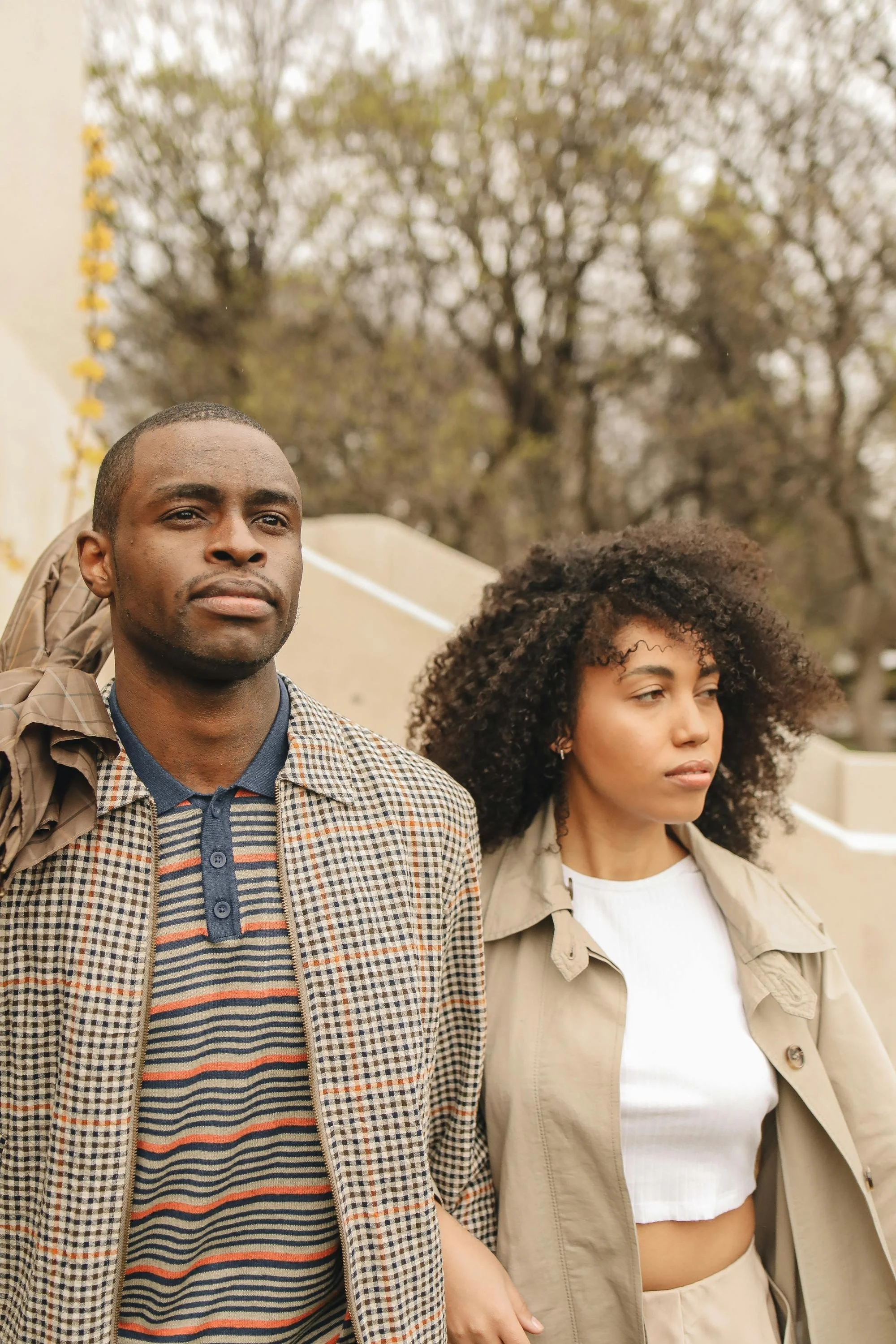 A couple walking outdoors on a cloudy day with trees in the background.