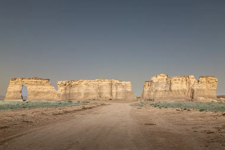 A dirt road leading toward large sandstone rock formations under a clear sky.