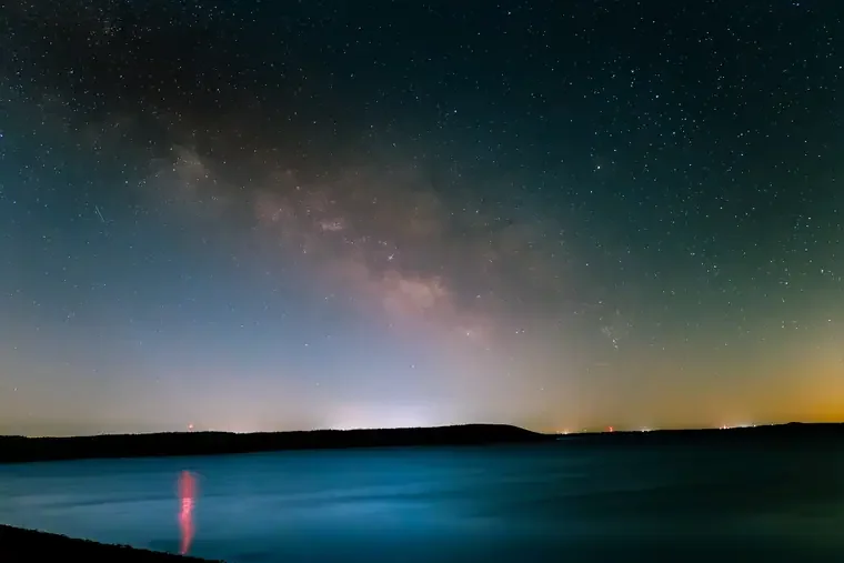 Night sky filled with stars and the Milky Way galaxy over a body of water with a distant horizon.
