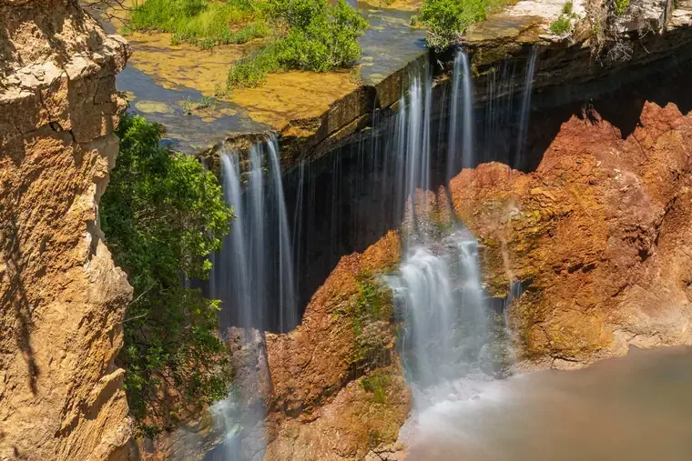 Waterfall flowing over cliff with greenery and rocky formations