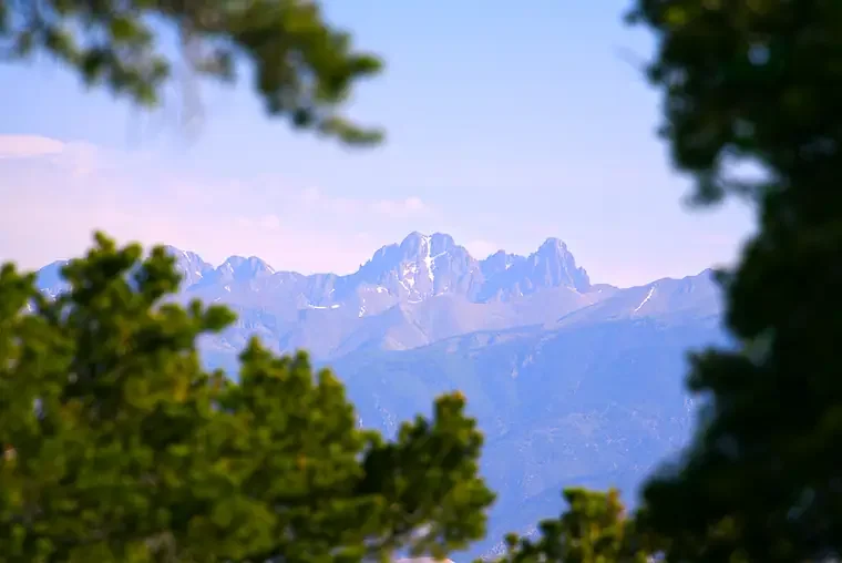 Mountain range viewed through green trees and foliage.