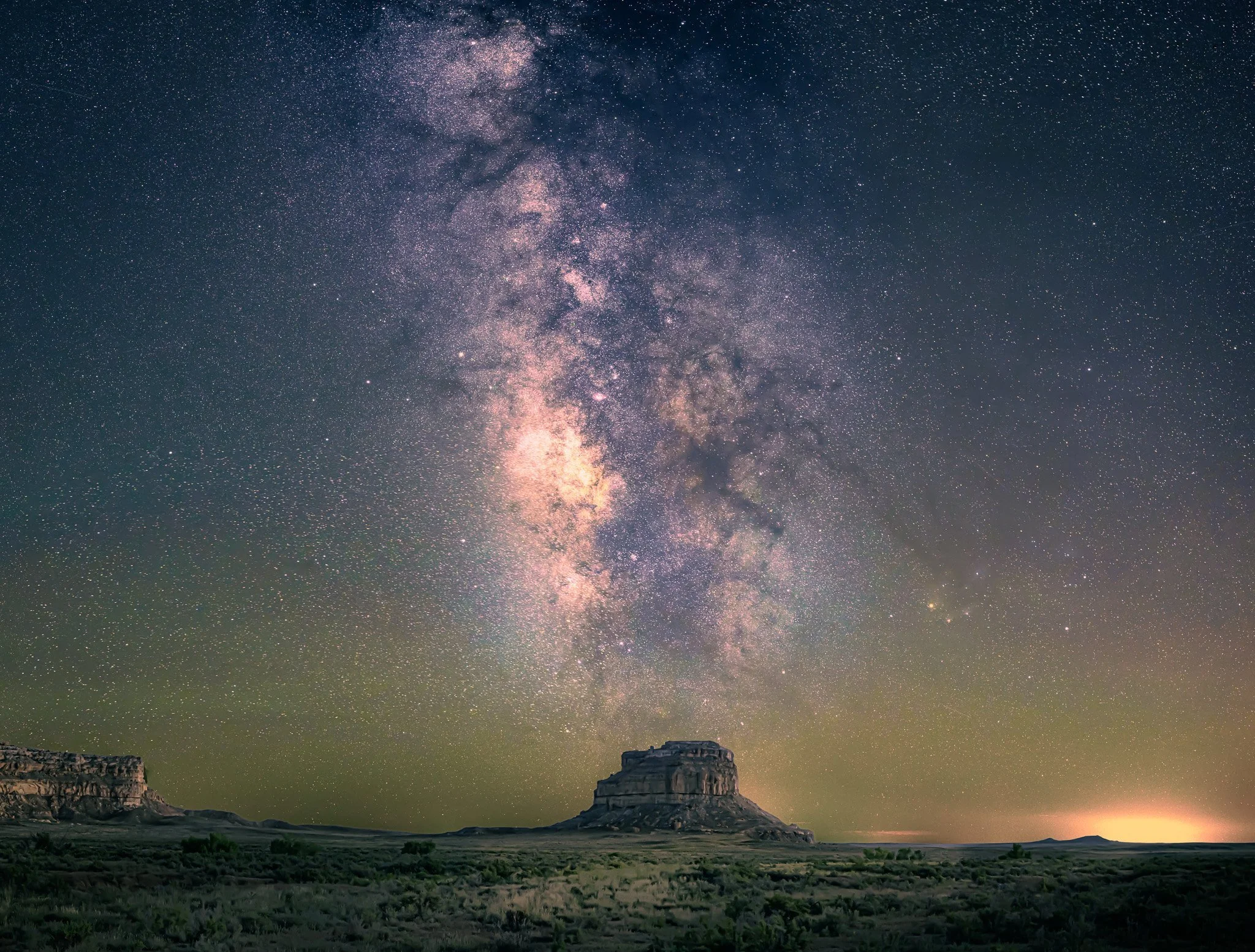 Night sky filled with numerous stars and visible Milky Way galaxy above a desert landscape with rock formations