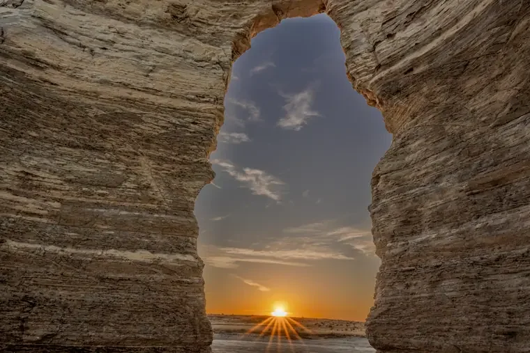View of a sunset seen through a natural rock arch formation.