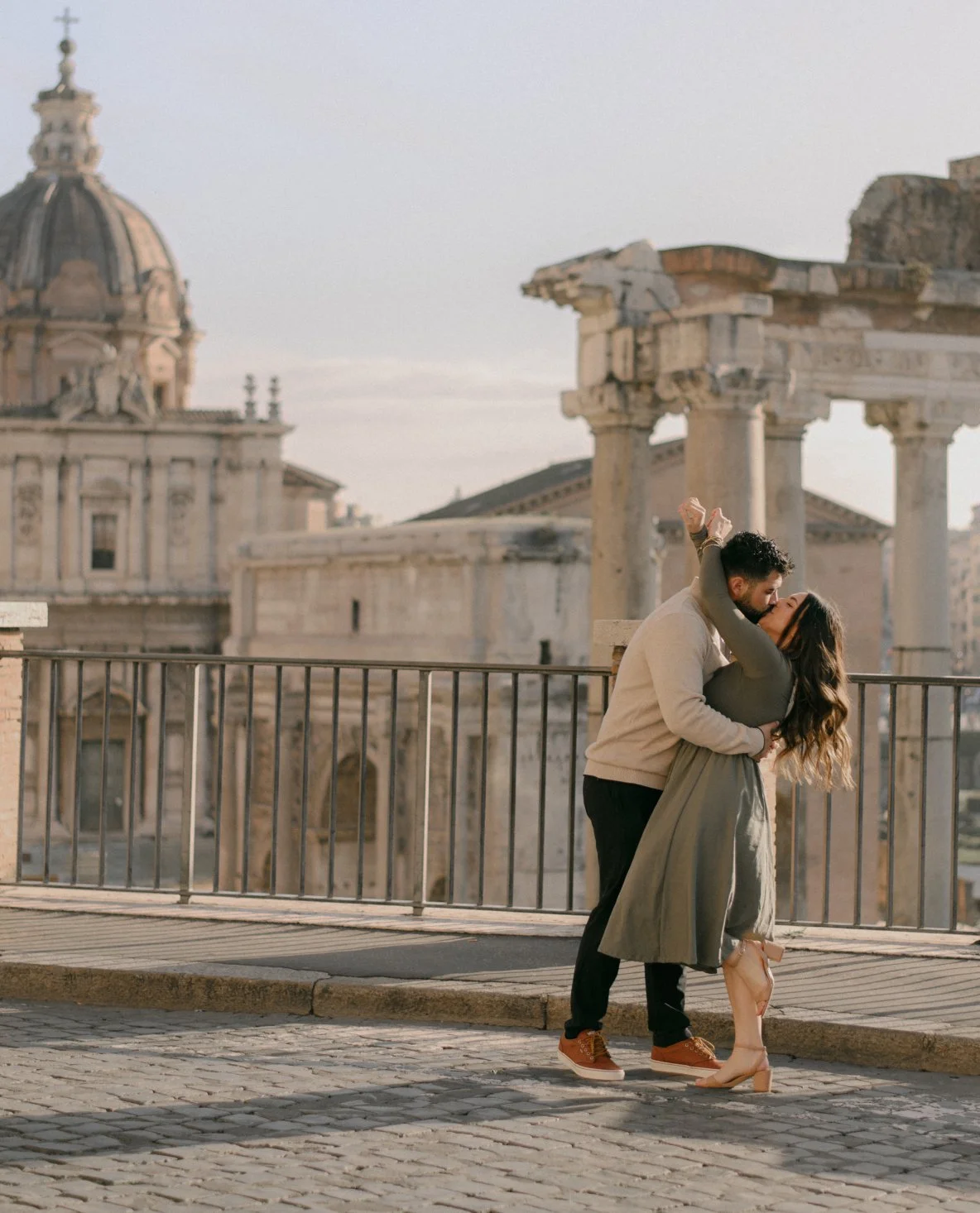 A couple sharing a kiss on a rooftop with ancient ruins and historic buildings in the background