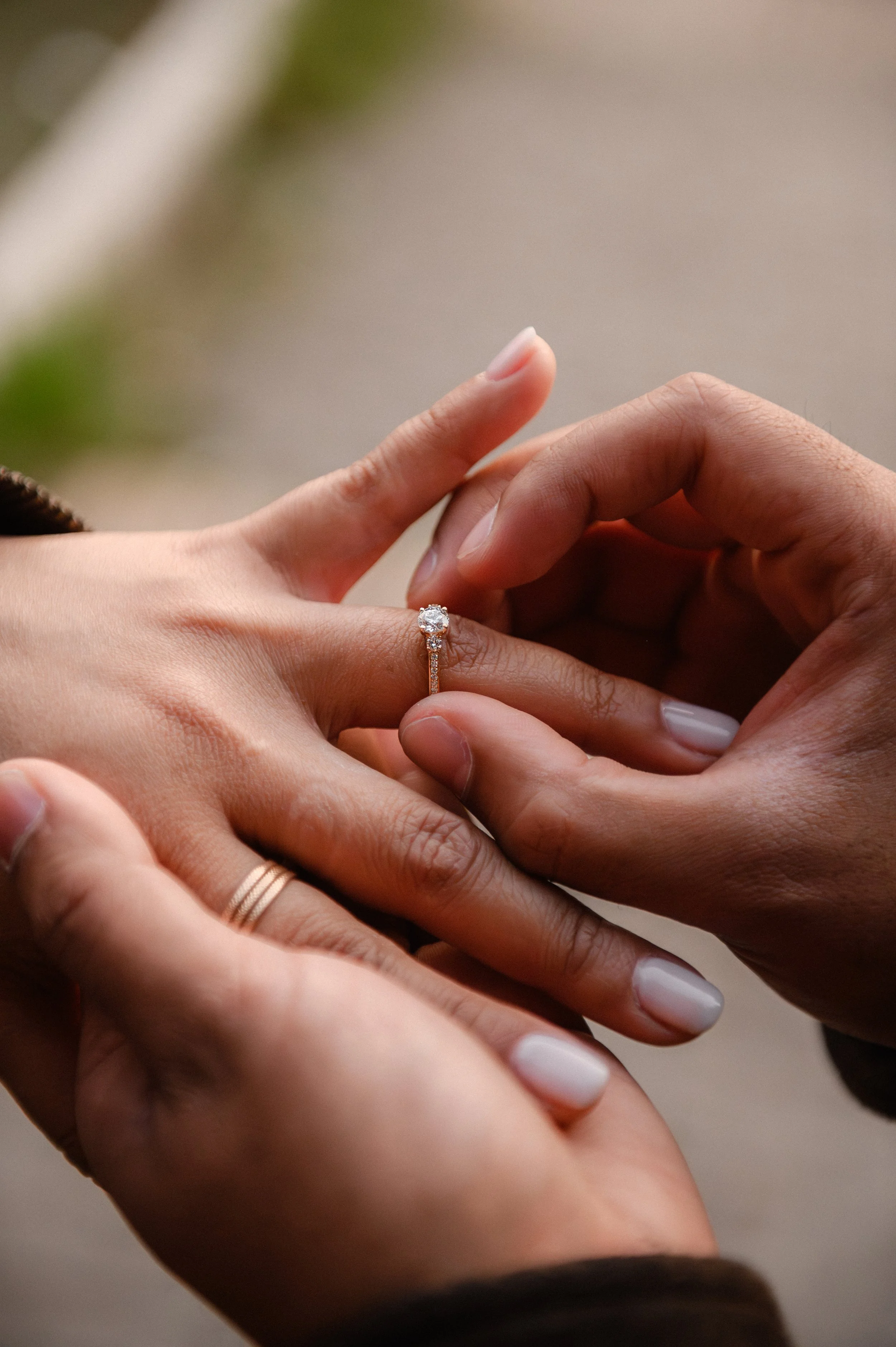Close-up of a person placing a diamond engagement ring on another person's finger during a marriage proposal.