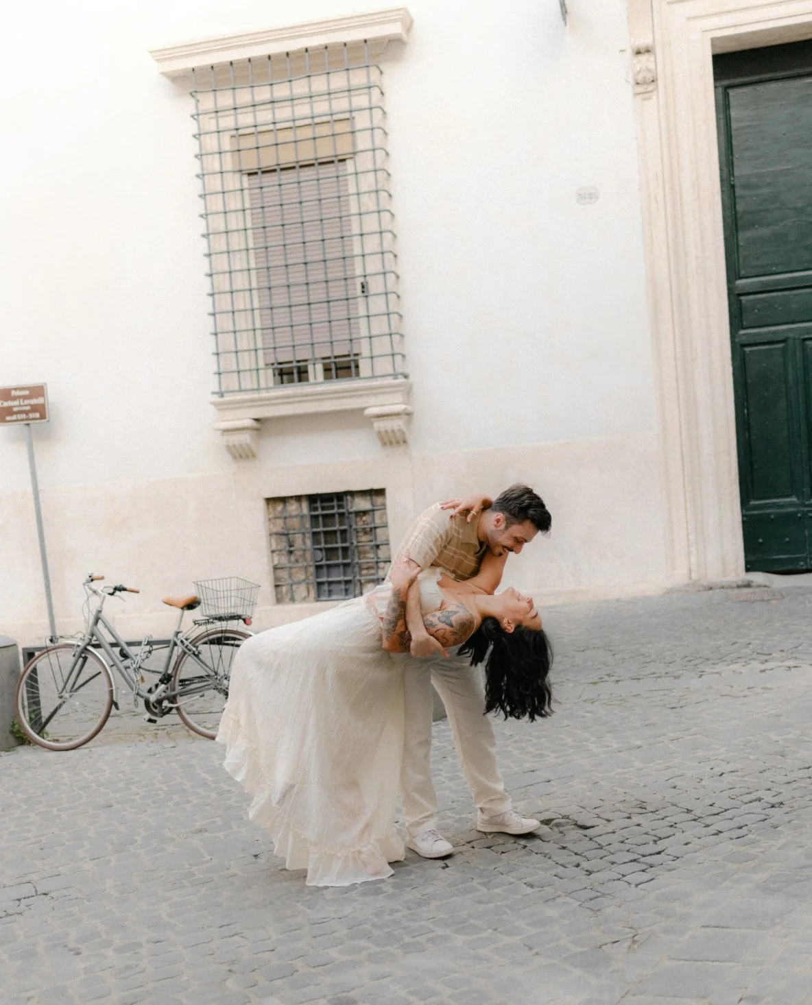 A couple dancing on a cobblestone street, the man is holding the woman as she leans back, both dressed in casual clothing.