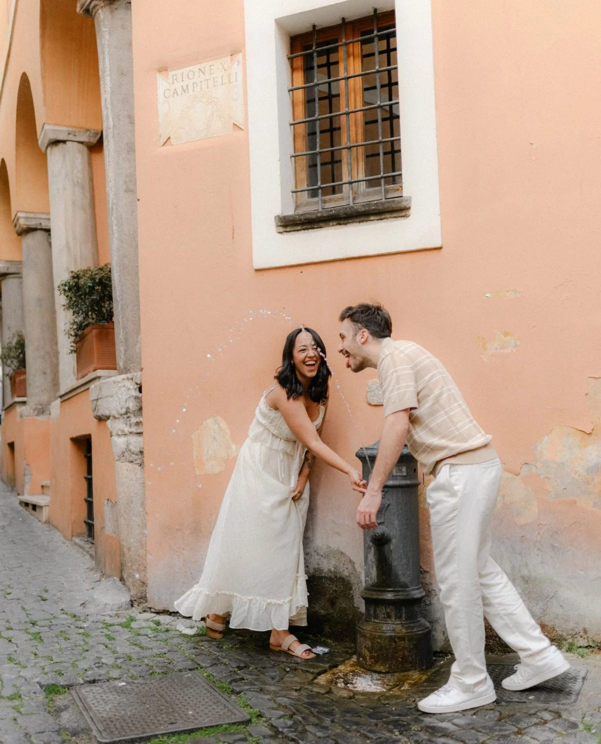 Couple laughing near fountain in Rome street, playful candid photoshoot