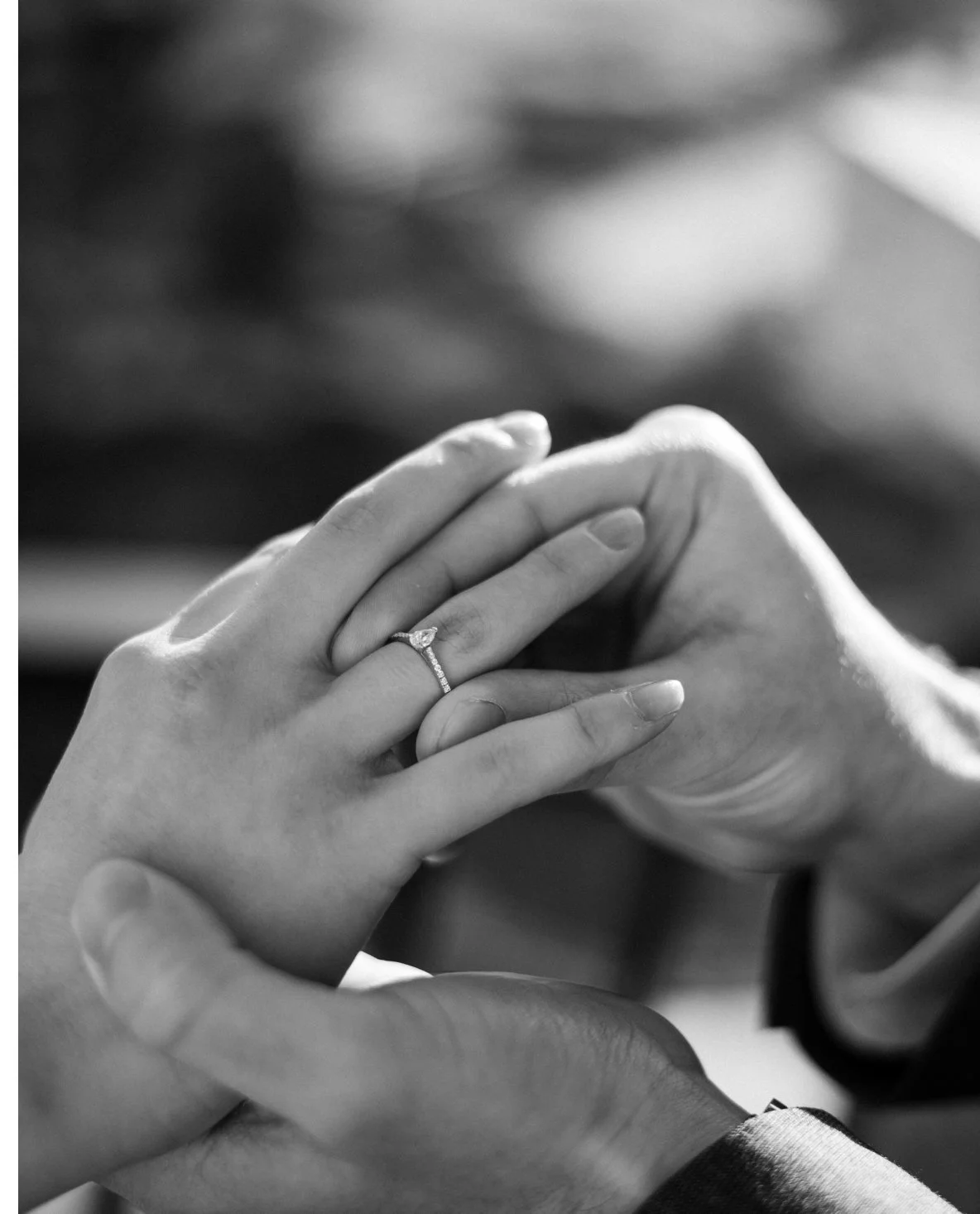 Close-up of a couple holding hands, with the woman’s hand showing an engagement ring, in black and white.