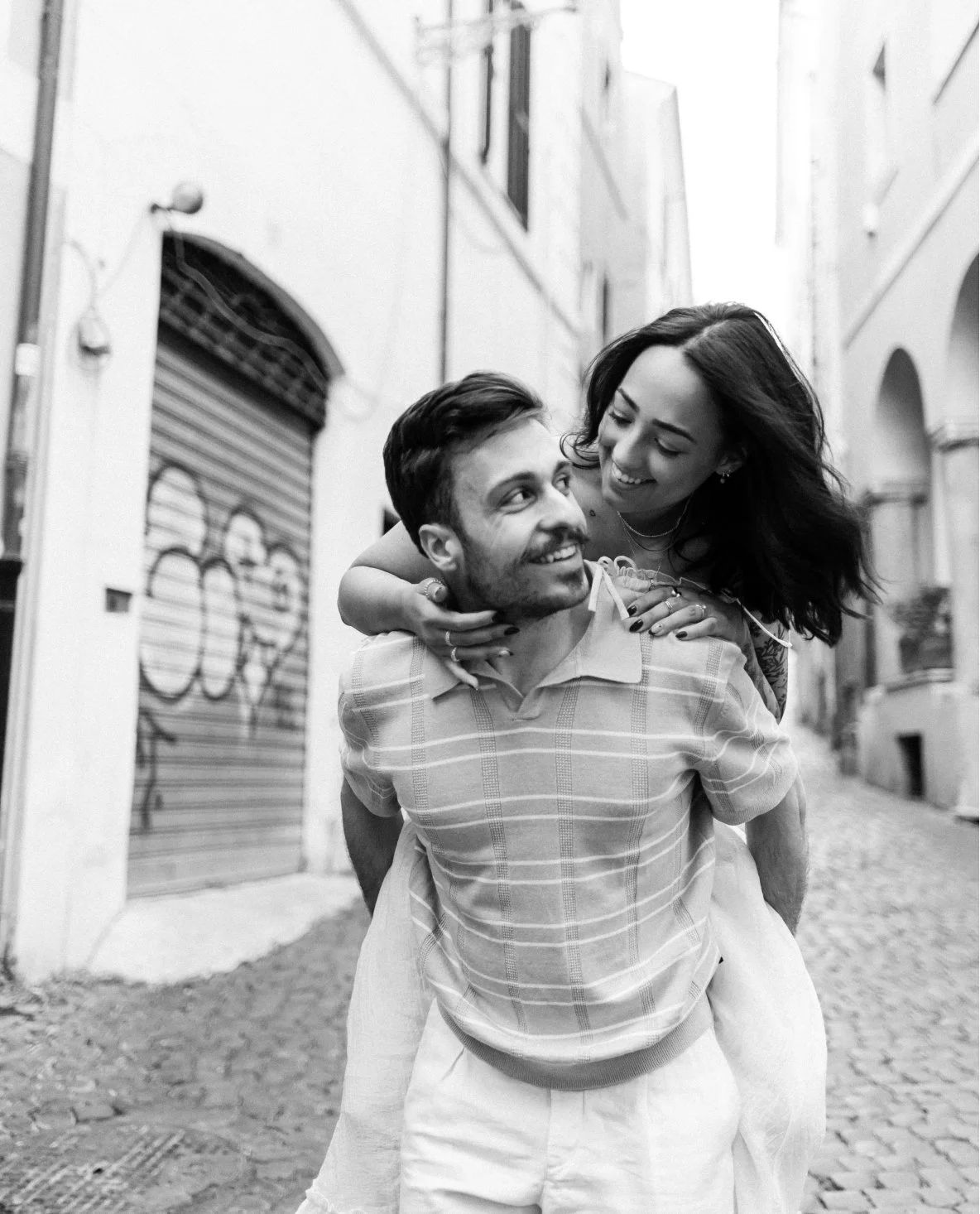 A happy couple, a man and woman, enjoying an embrace on a cobblestone street in a European city, black and white photograph.