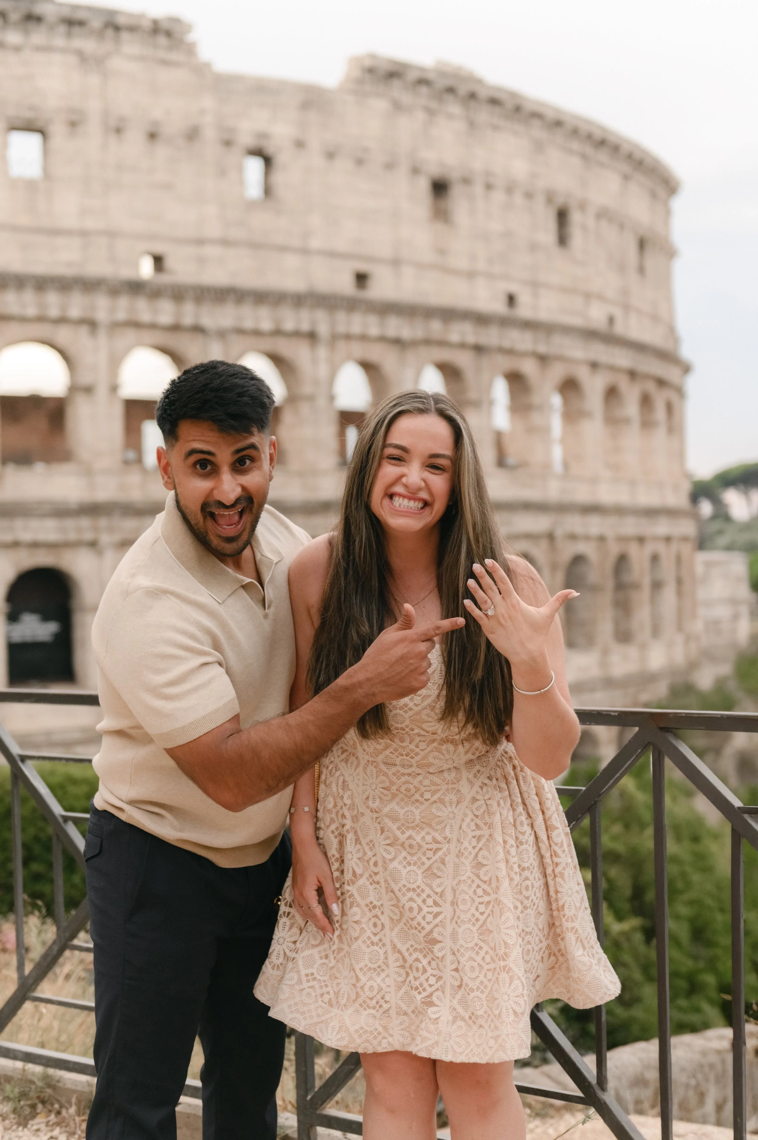 A smiling couple shows off an engagement ring in front of the Colosseum in Rome, Italy.