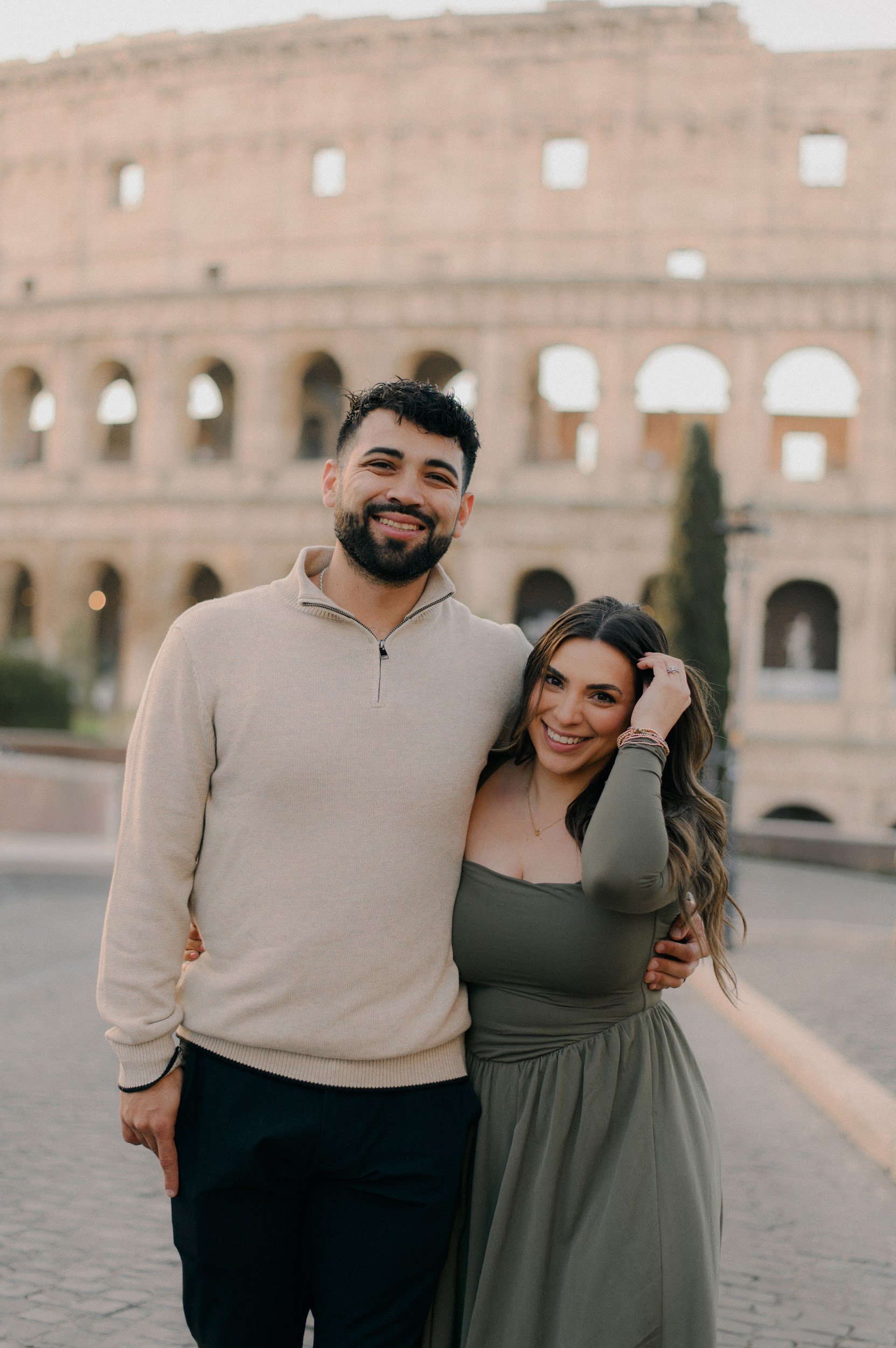 A smiling man and woman standing close together in front of the Colosseum in Rome, Italy.