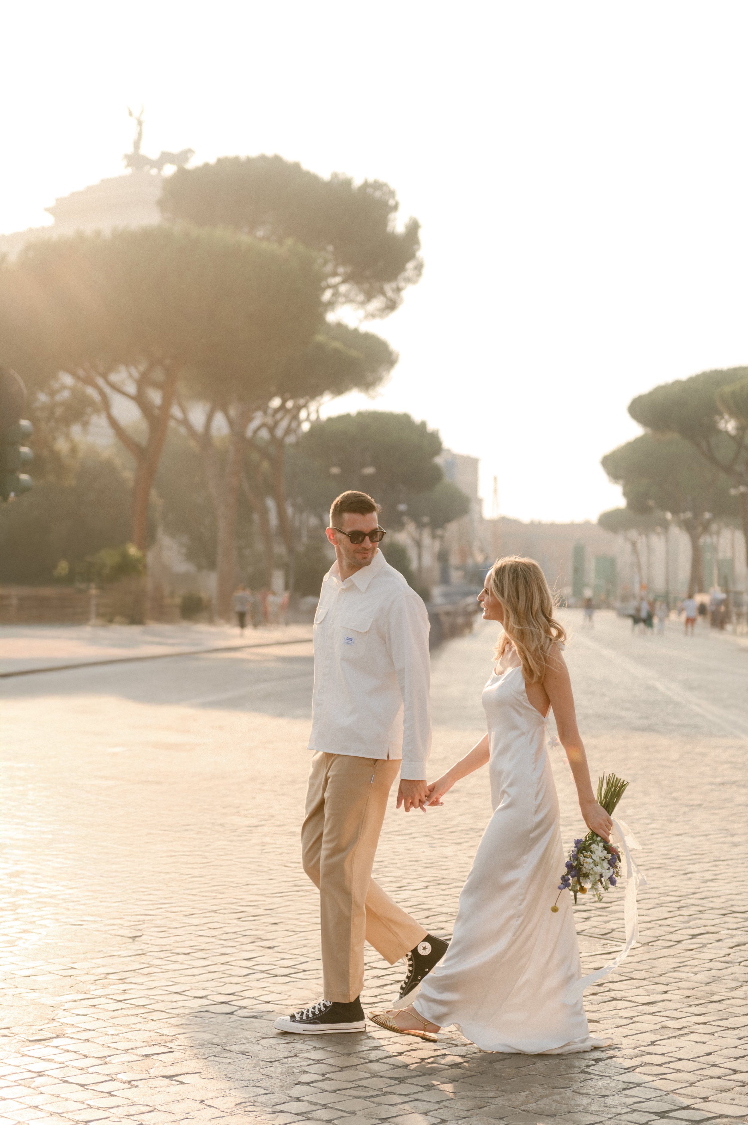 A couple holding hands walking on a cobblestone street at sunset in Rome, during wedding photoshoot