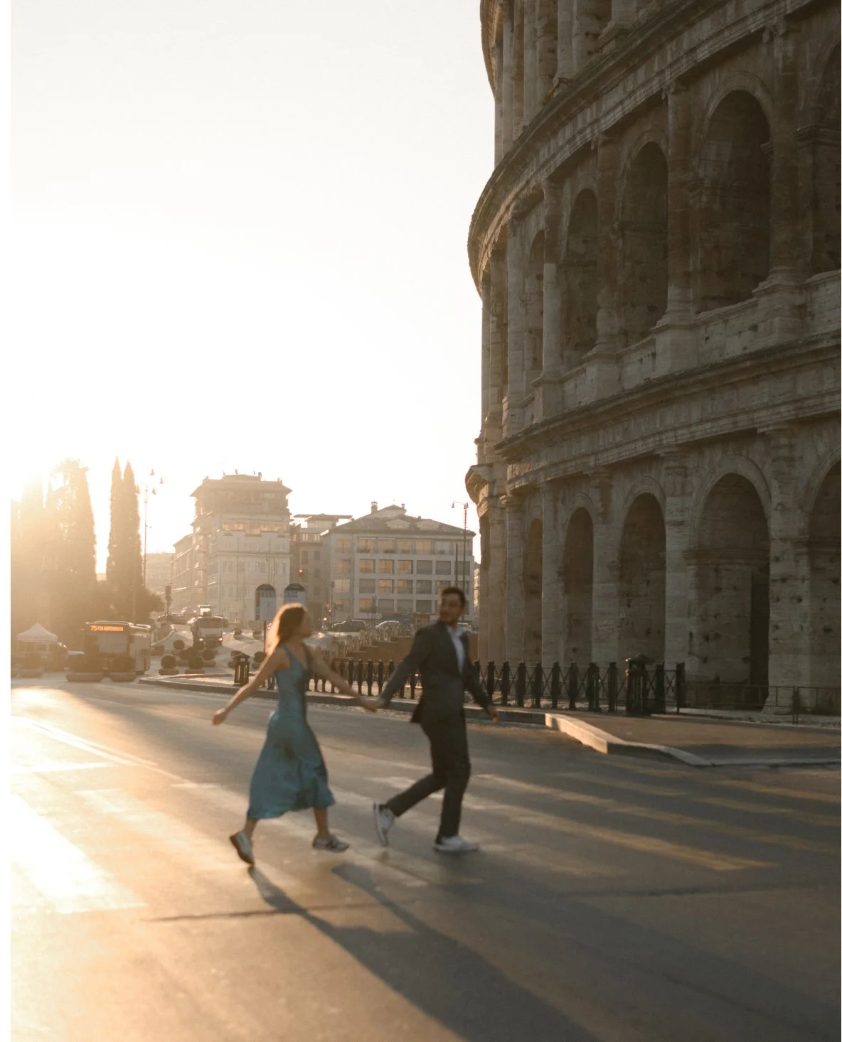 A couple holding hands and walking across a street near the Colosseum in Rome during sunset.