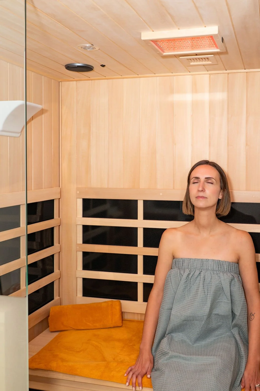 Woman sitting in an infrared sauna. She is in the lower right-hand corner of the photo with her eyes closed and a relaxed look on her face.