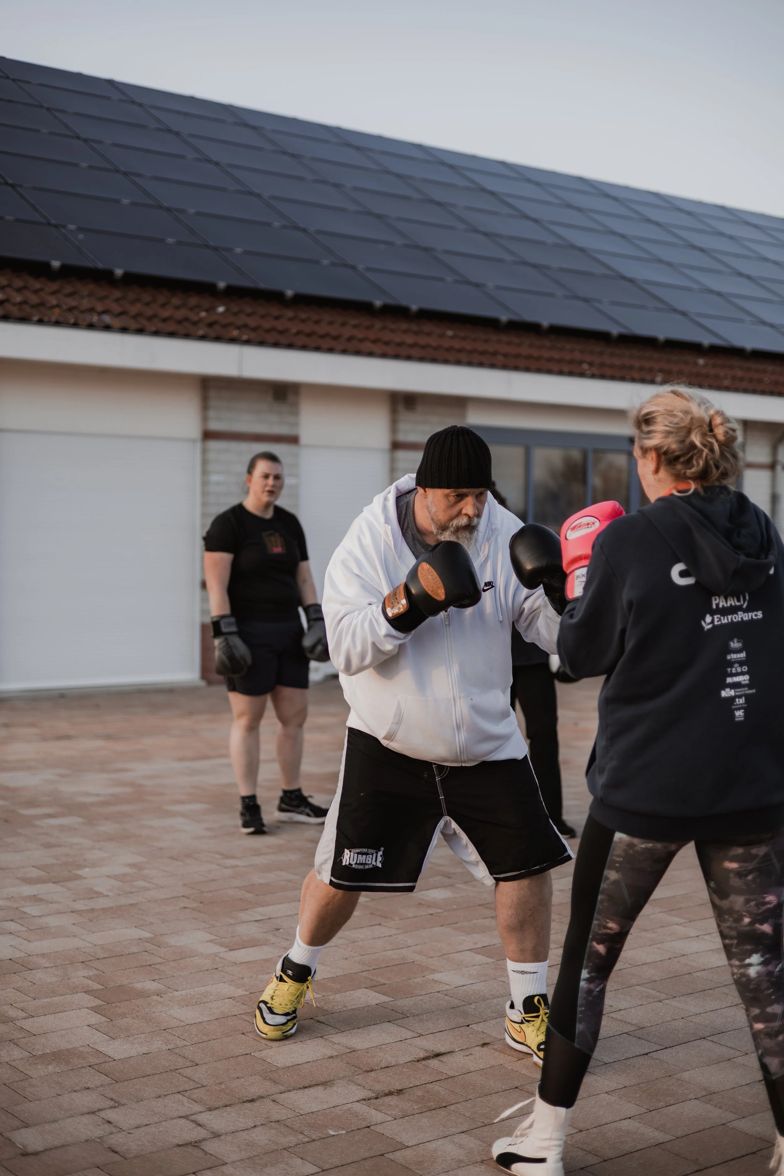 Vijf mensen die aan boxing training doen buiten, met een house met zonnepanelen op het dak op de achtergrond.