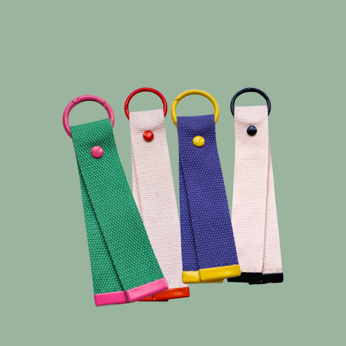 Vier bunte Schlüsselbänder mit Metallringen in Pink, Rot, Gelb und Schwarz auf grünem Hintergrund.