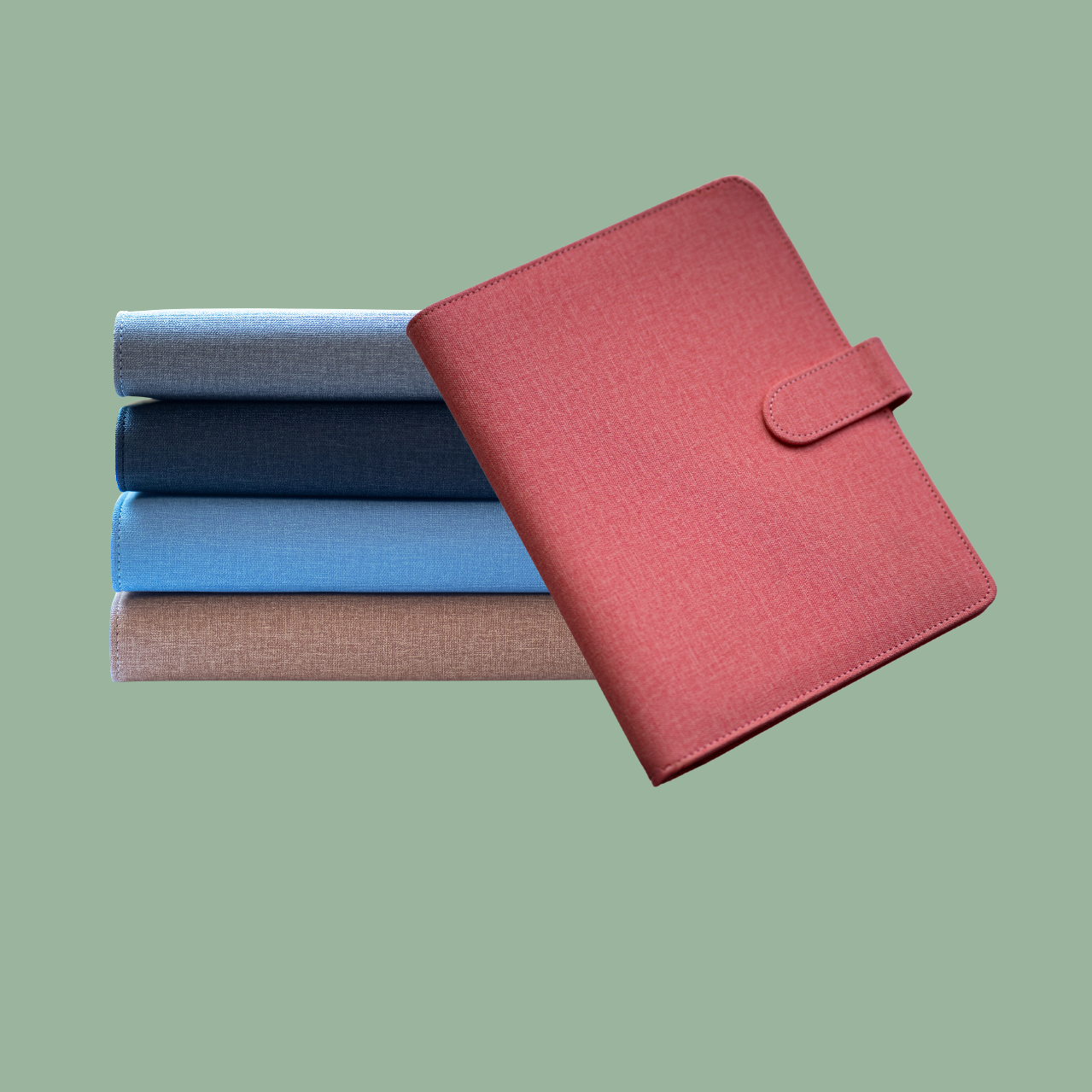 Ein Stapel bunter Stoffbücher und ein rot gefärbtes Notizbuch mit Klettverschluss auf grünem Hintergrund.