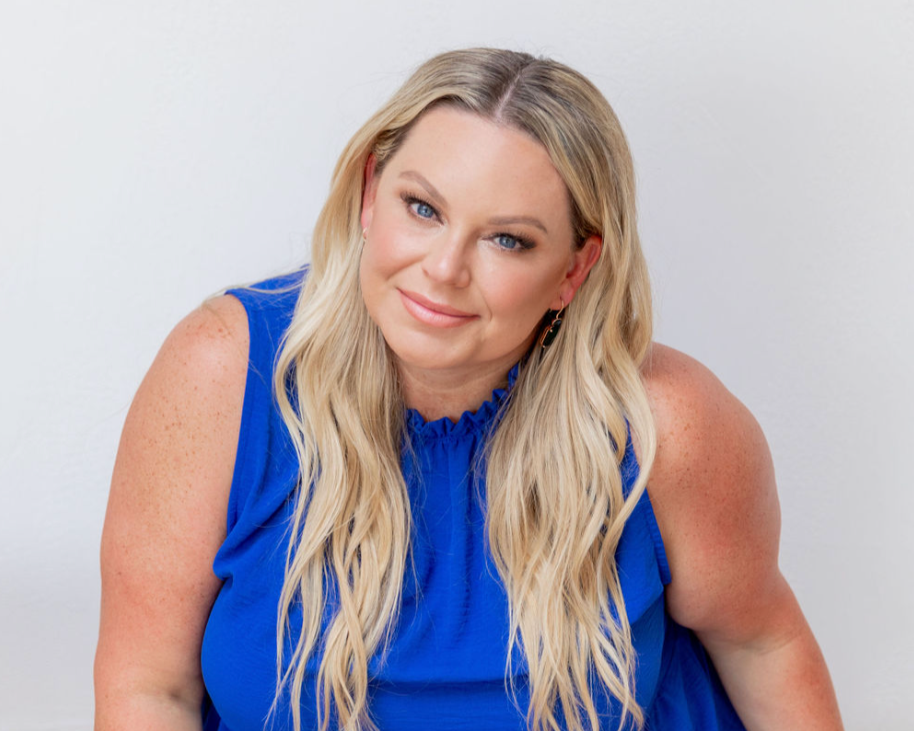 A woman with long blonde hair wearing a blue sleeveless top, smiling at the camera against a plain white background.