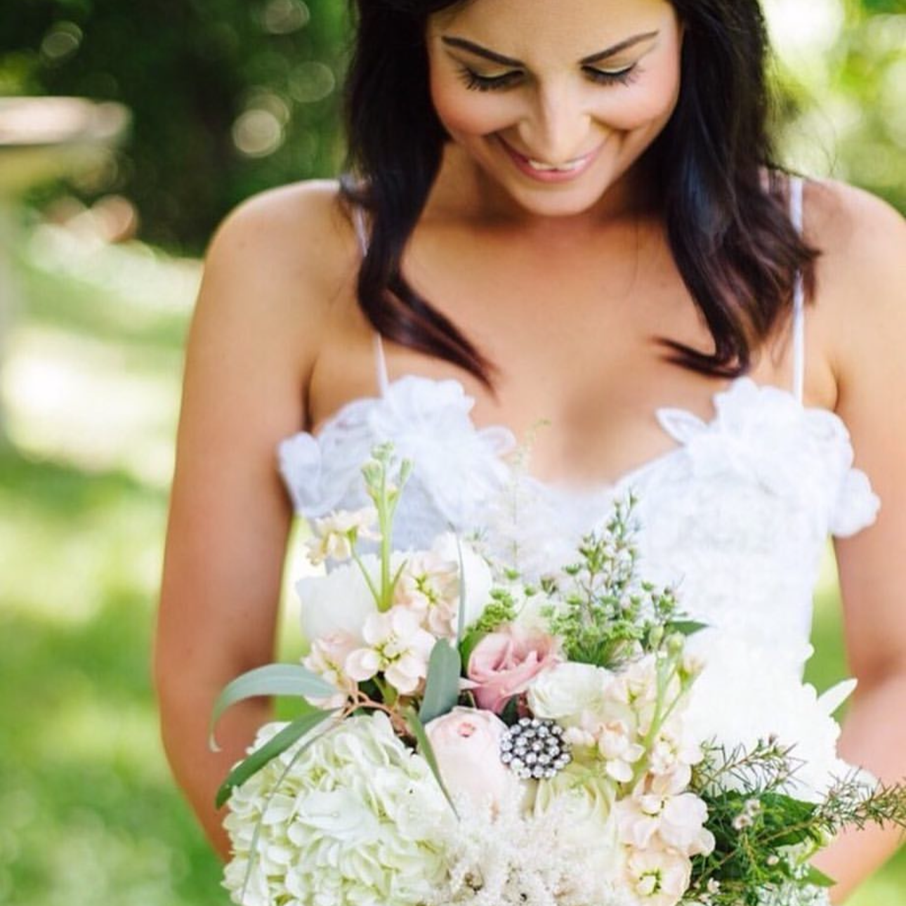 A woman in a white dress looking down at a bouquet of flowers she is holding.