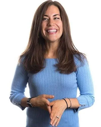 A woman with long brown hair smiling and looking to the side, wearing a blue ribbed sweater and a black watch.