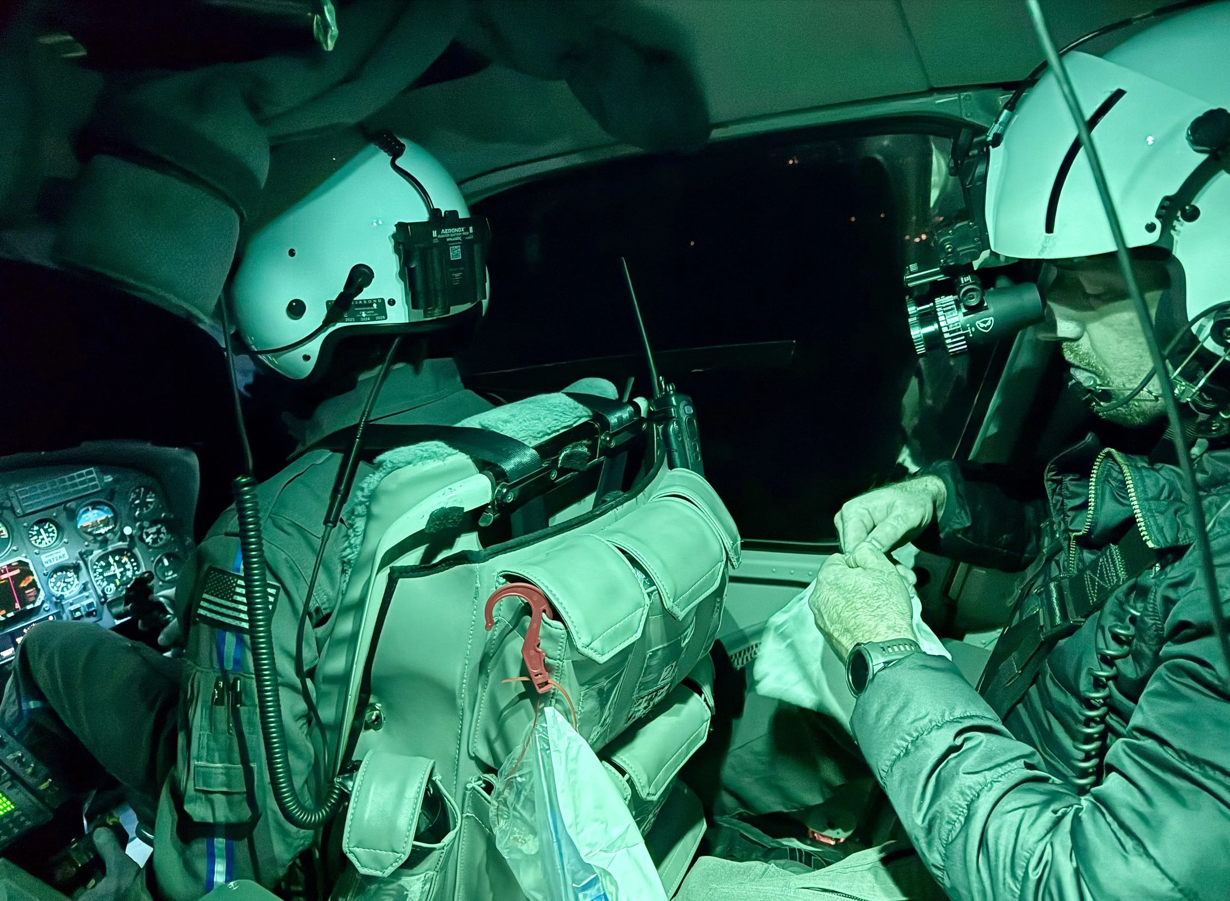 Two pilots sitting in the cockpit of a helicopter at night, shaking hands.