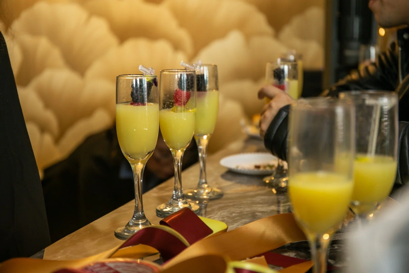 Varios copas de champagne con bebida de color amarillo y frutas decorativas en una celebración