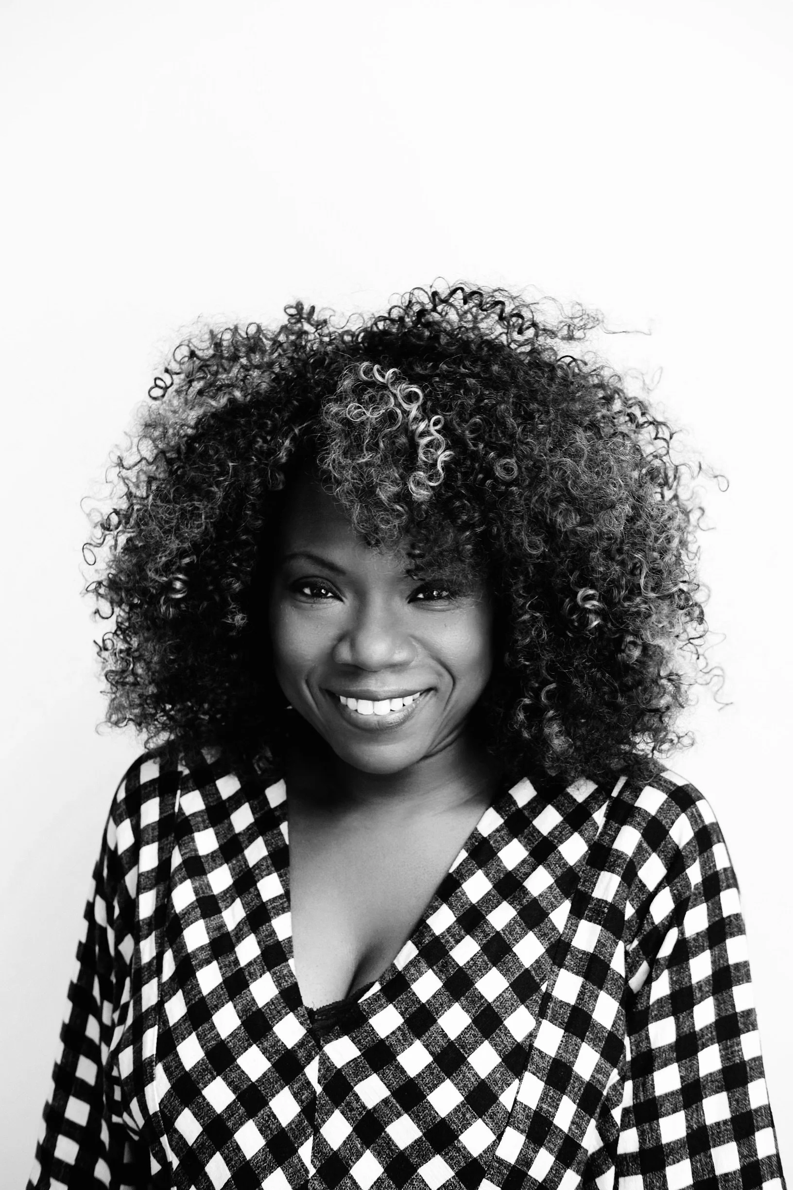 Smiling woman with curly hair in black and white checkered top.