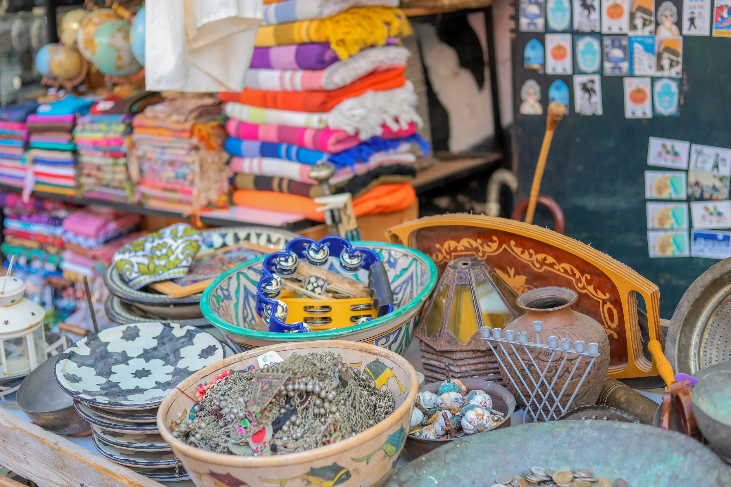 Table of colorful jewelry, bowls, and vintage items with folded beach towels in the background at a flea market.