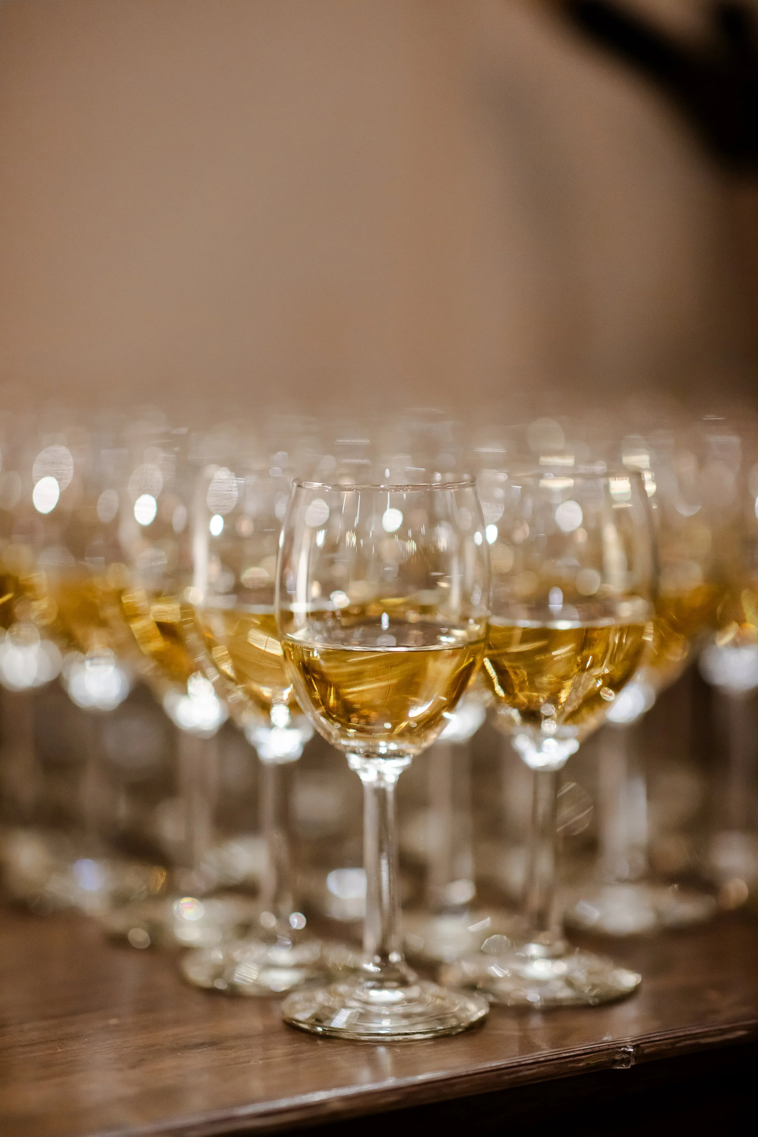 Multiple glasses of white wine on a wooden surface, with some in focus and others blurred in the background.
