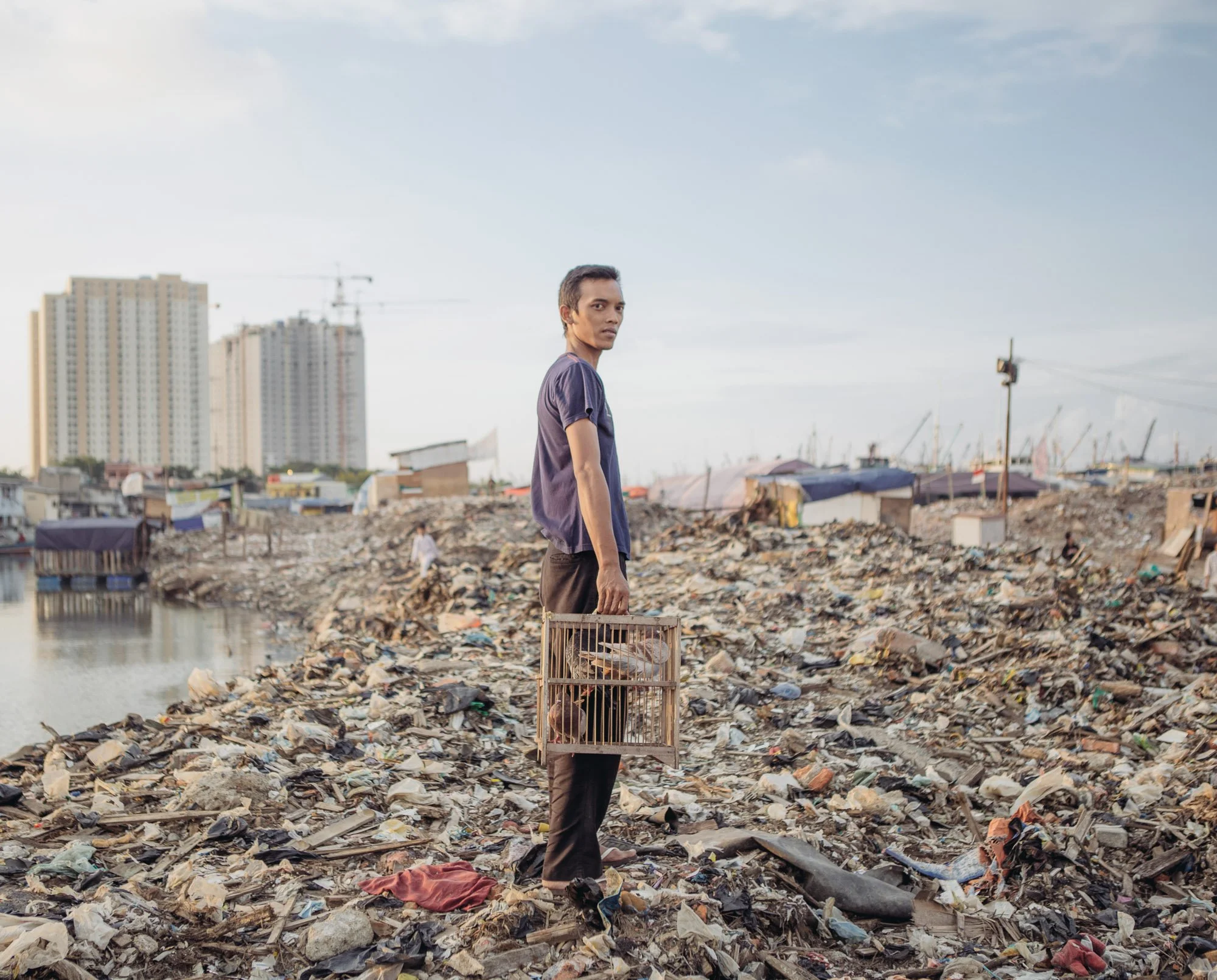 A man carrying a cage of pigeons poses for a photograph in the Pasar Ikan district of North Jakarta. 