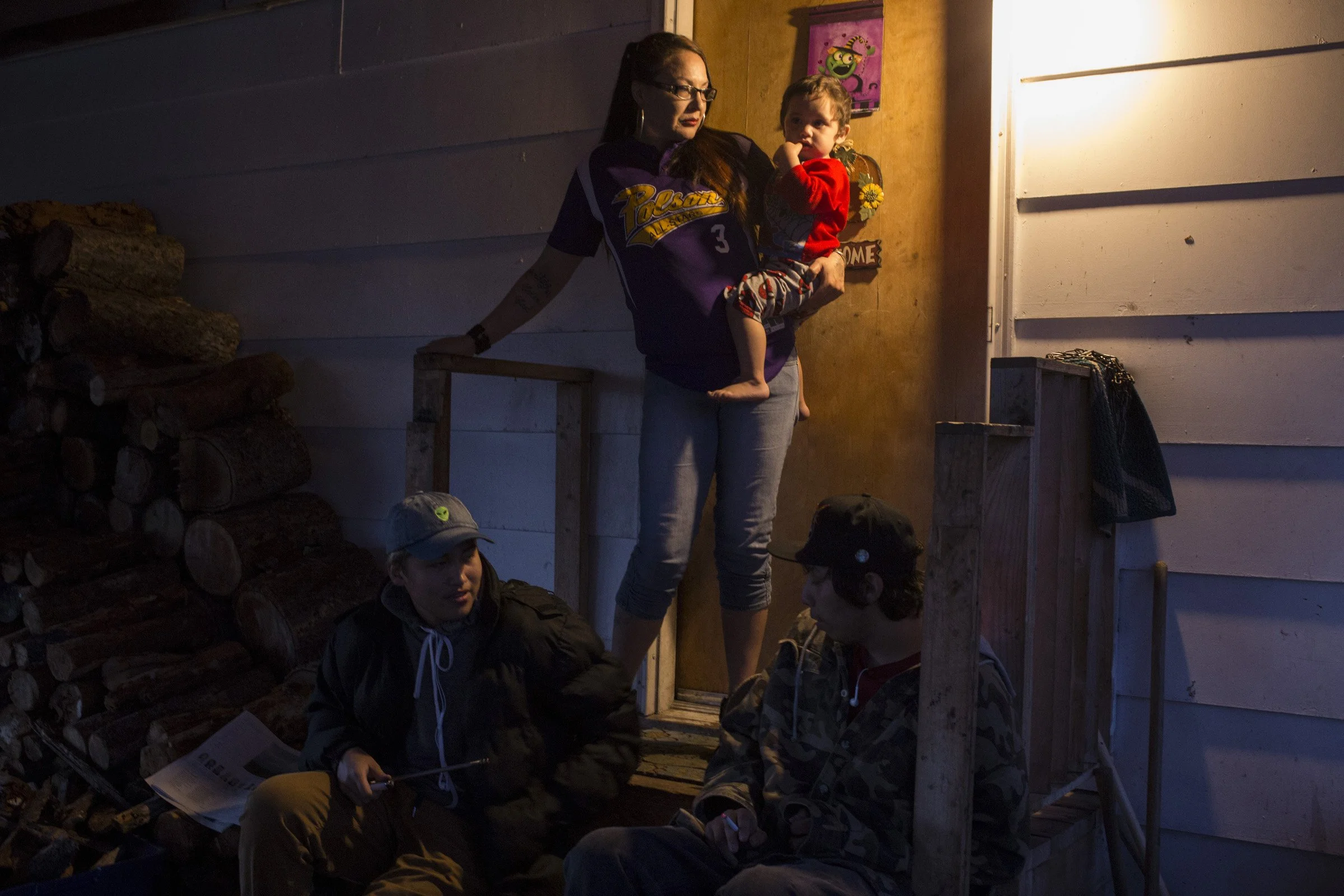  Susie Boushie, 37, looks out from her front porch while holding her grandson, Niste Omeasoo, 2, as two of her son’s friends sit on their porch at their home in Pablo, Montana, on Sunday, October 22, 2017. (Photo by Brittany Greeson) 