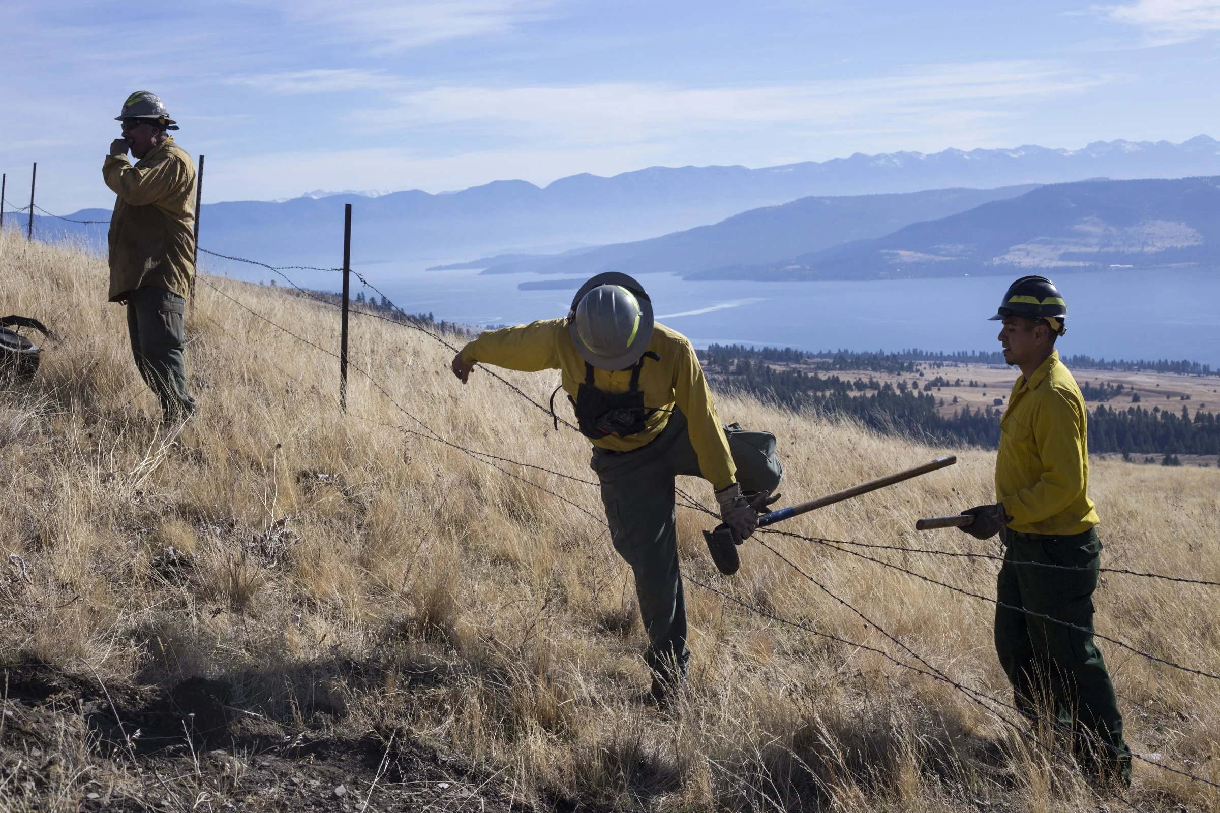  Members of the Confederated Salish and Kootenai Tribes Division of Fire cross over a barbed wire fence after preparing a barrier for a prescribed burn just along a ridge line outside of Elmo, Montana, on Tuesday, October 24, 2017. (Photo by Brittany