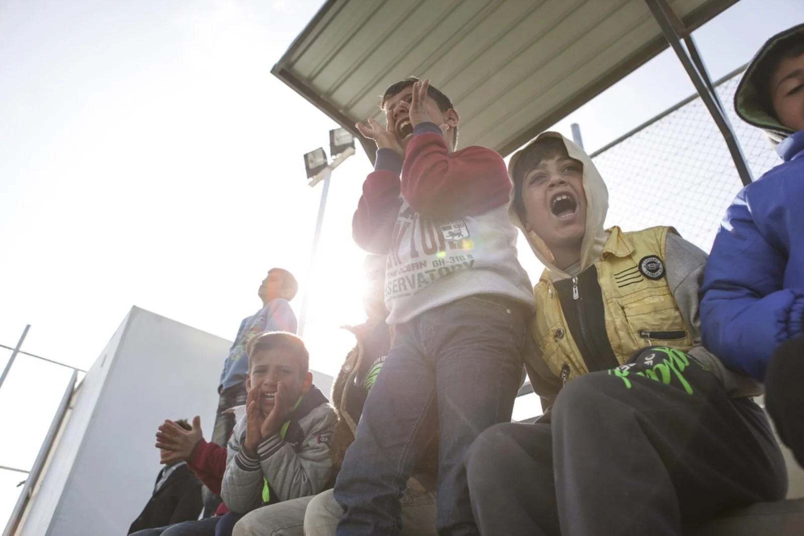  A group of refugee children cheer as they watch their peers play soccer on one of the pitches provided by World Vision at Azraq refugee camp. Recreation soccer teams are formed in order to provide a better quality of life for the children living in 