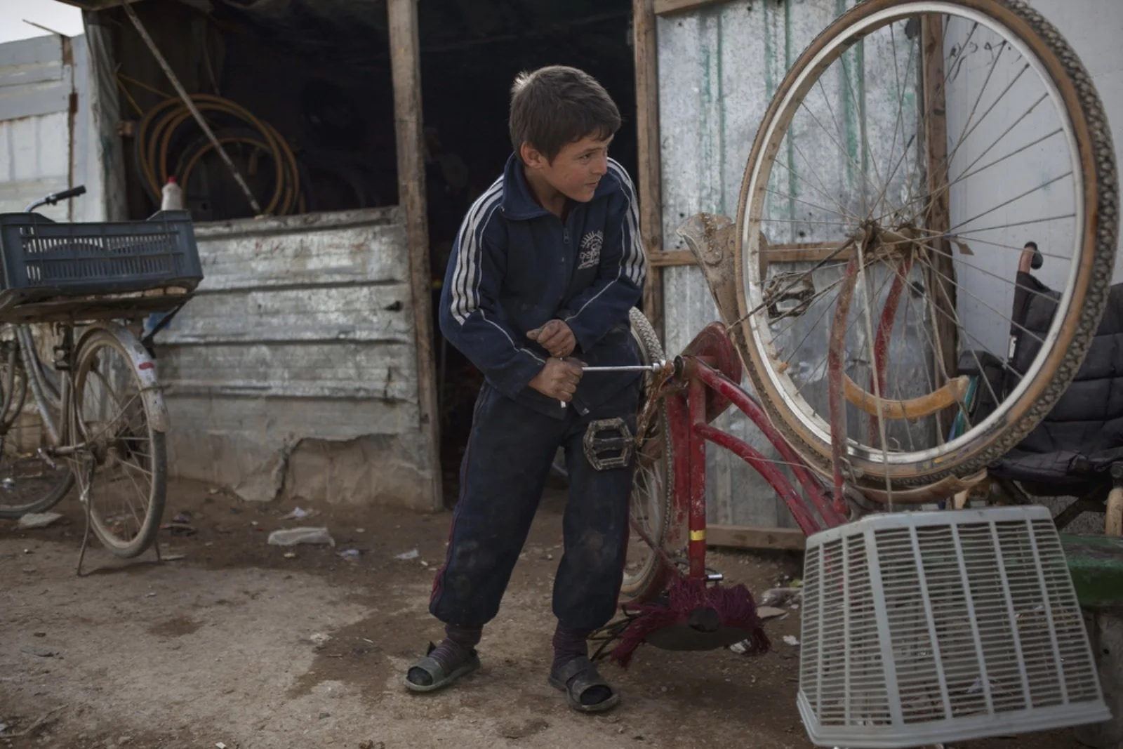  Ebraham Alatmia, 11, a Syrian refugee from Daraa, fixes a bicycle in a makeshift bike shop where he works in the main marketplace of Zaatari. (Christopher Lee/GroundTruth) 
