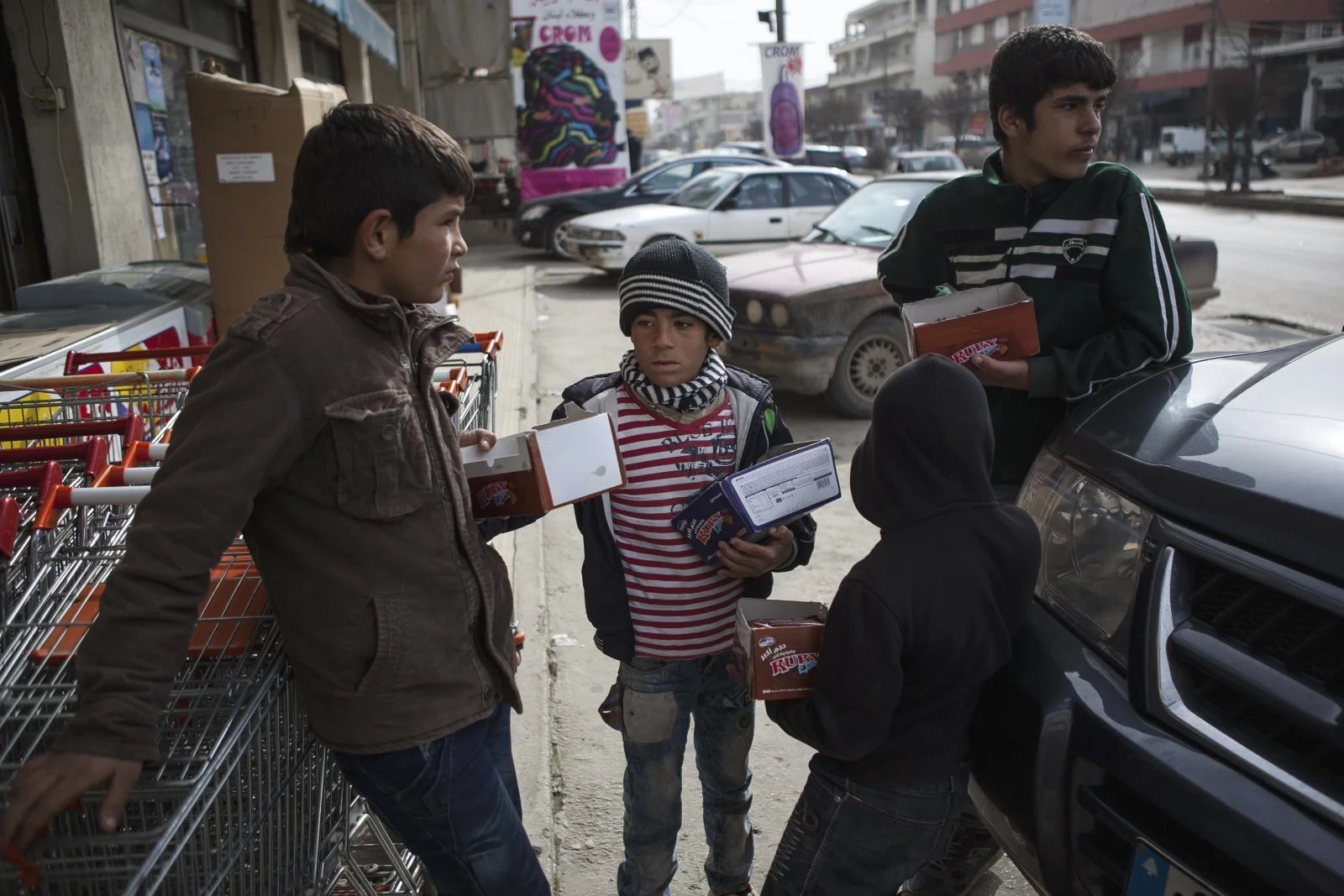  Khaled (left), 12, Mahmut (center), 8, and Ahmed (right), 15, brothers and refugees from Homs, wait for customers to come out of a grocery story while selling biscuits in the Bekaa Valley while selling biscuits. (Christopher Lee/GroundTruth) 