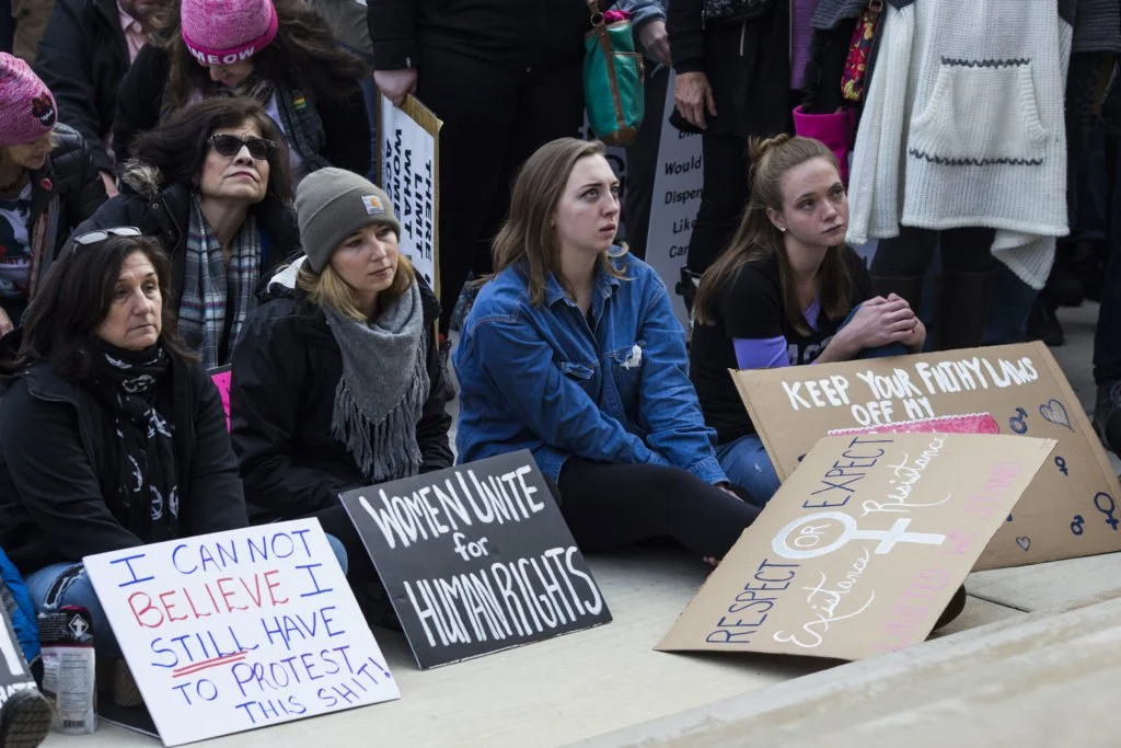   Young women sit along the steps outside of the Michigan State Capitol as a representative of Planned Parenthood speaks about the possible funding losses under the new presidential administration, during the Women’s March on Lansing in Lansing, Mich