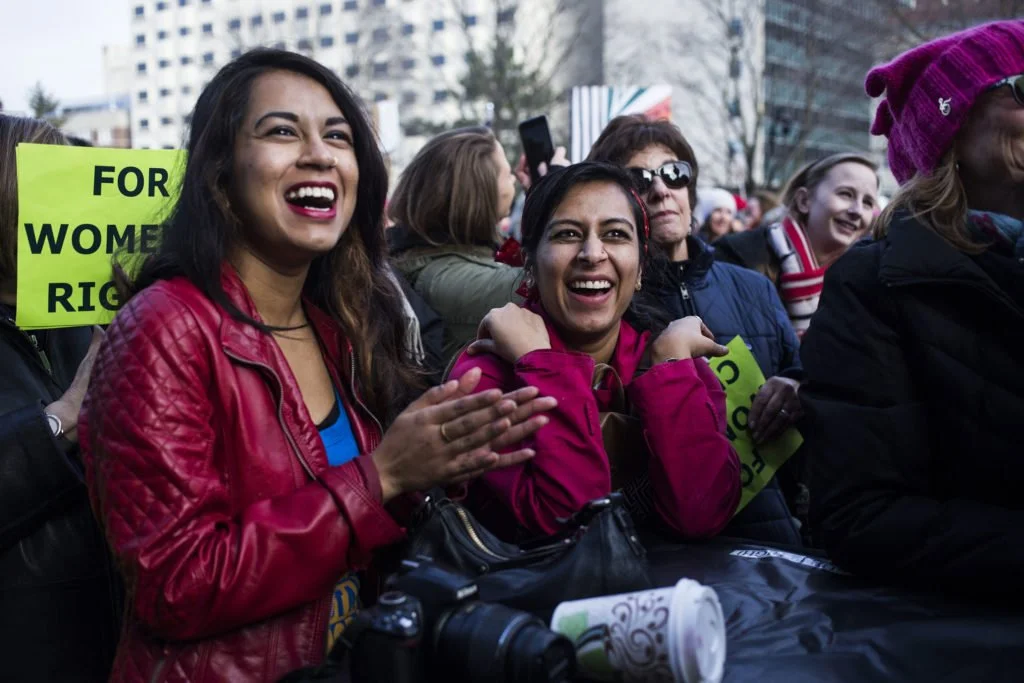   Sharmin Begum, 23, right, and Tahrima Khanom, 26, left, both of Hamtramck, Mich., laugh at a speaker’s remarks during the Women’s March outside of the Michigan State Capitol Building in Lansing, Mich., on Saturday, January 21, 2017. (Photo by Britt
