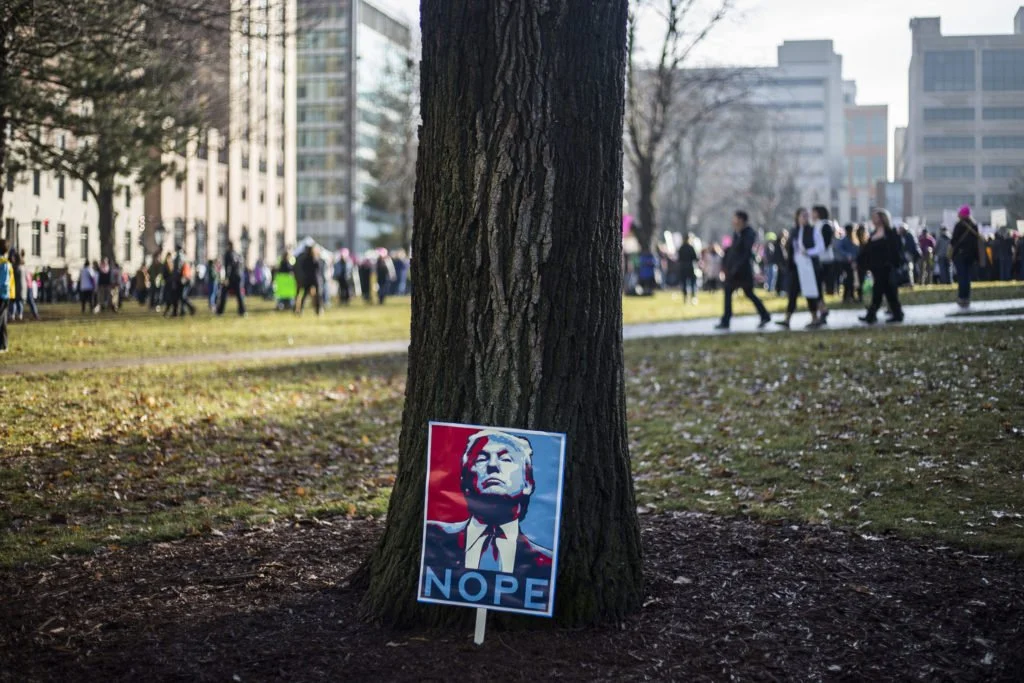   A sign leans against a tree outside of the Michigan State Capitol Building as attendees begin to return home from the Women’s March in Lansing, Mich., on Saturday, January 21, 2017. (Photo by Brittany Greeson/GroundTruth)  