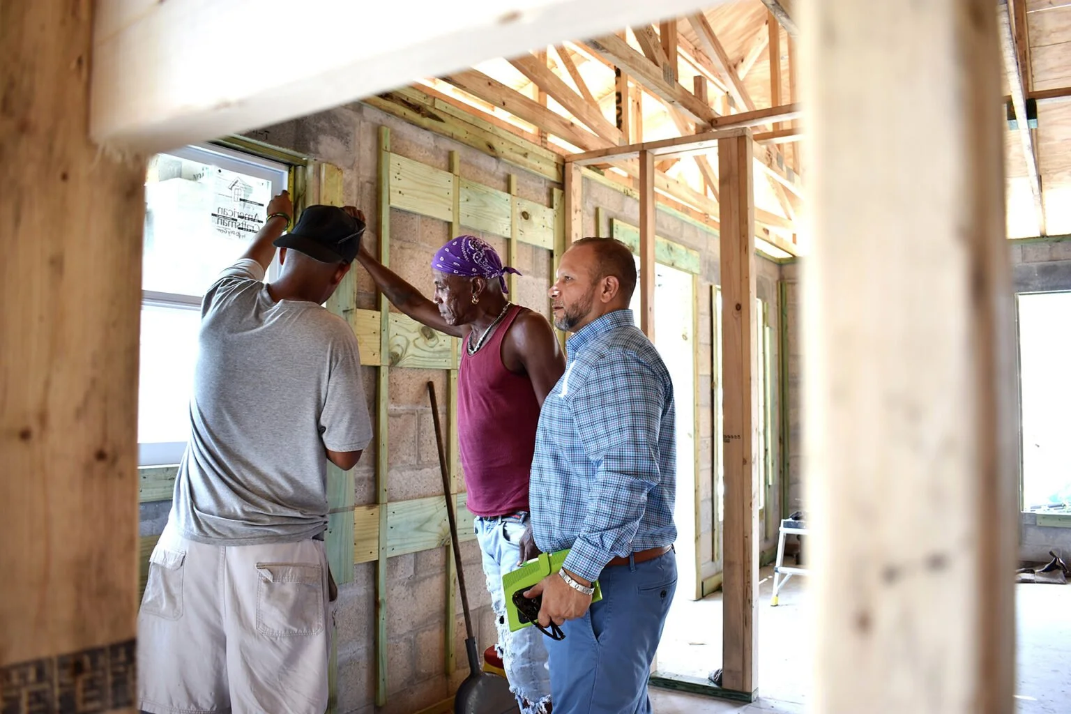   Tampa Bay Neighborhood Housing Services CEO Frank Cornier (center) inspects a window installation at a new-home build in Clearwater, Florida. He said the local housing agency has several standard floor plans that they replicate when building afford