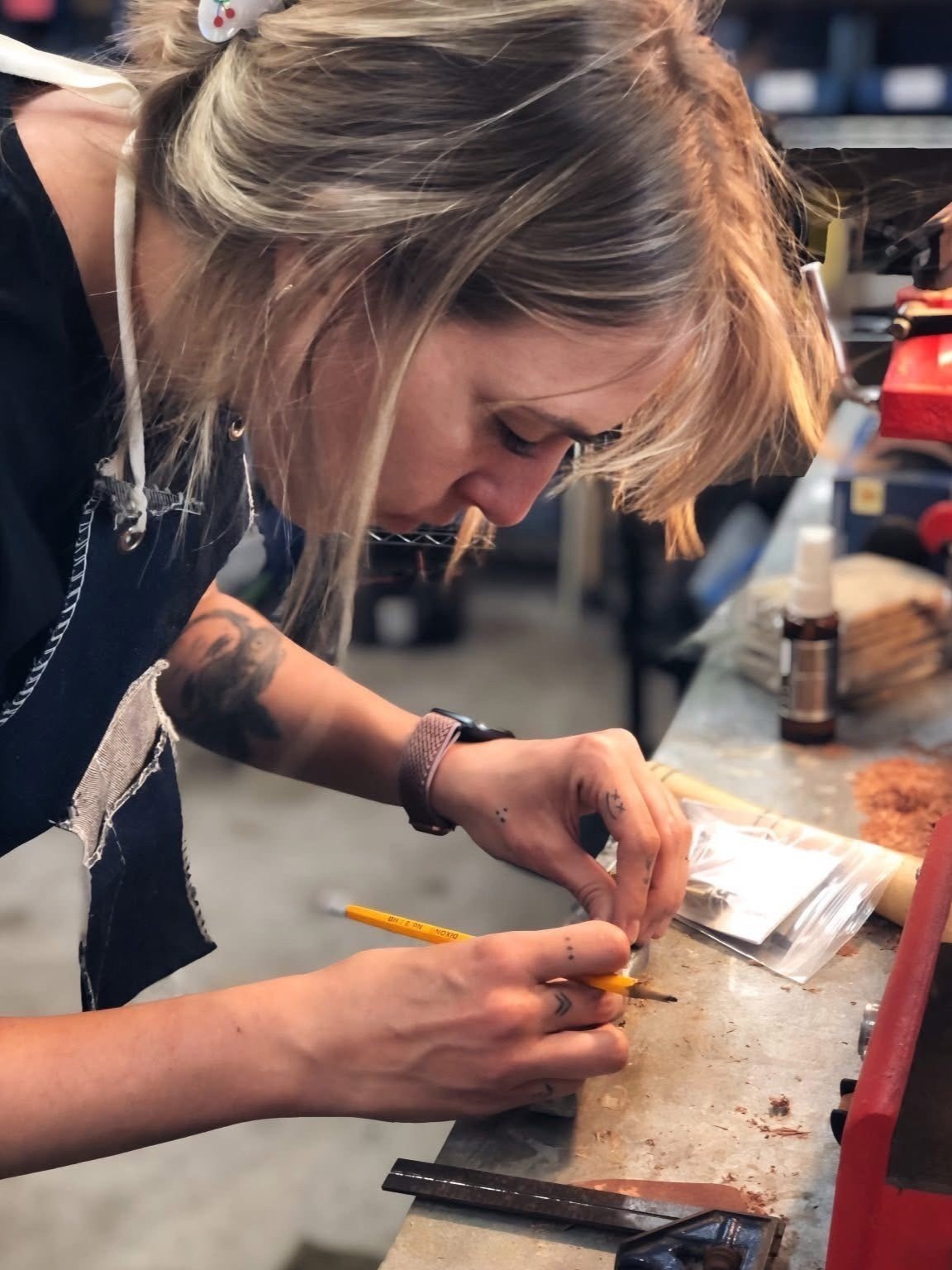 A woman working carefully on a small object at a cluttered workbench in a workshop.