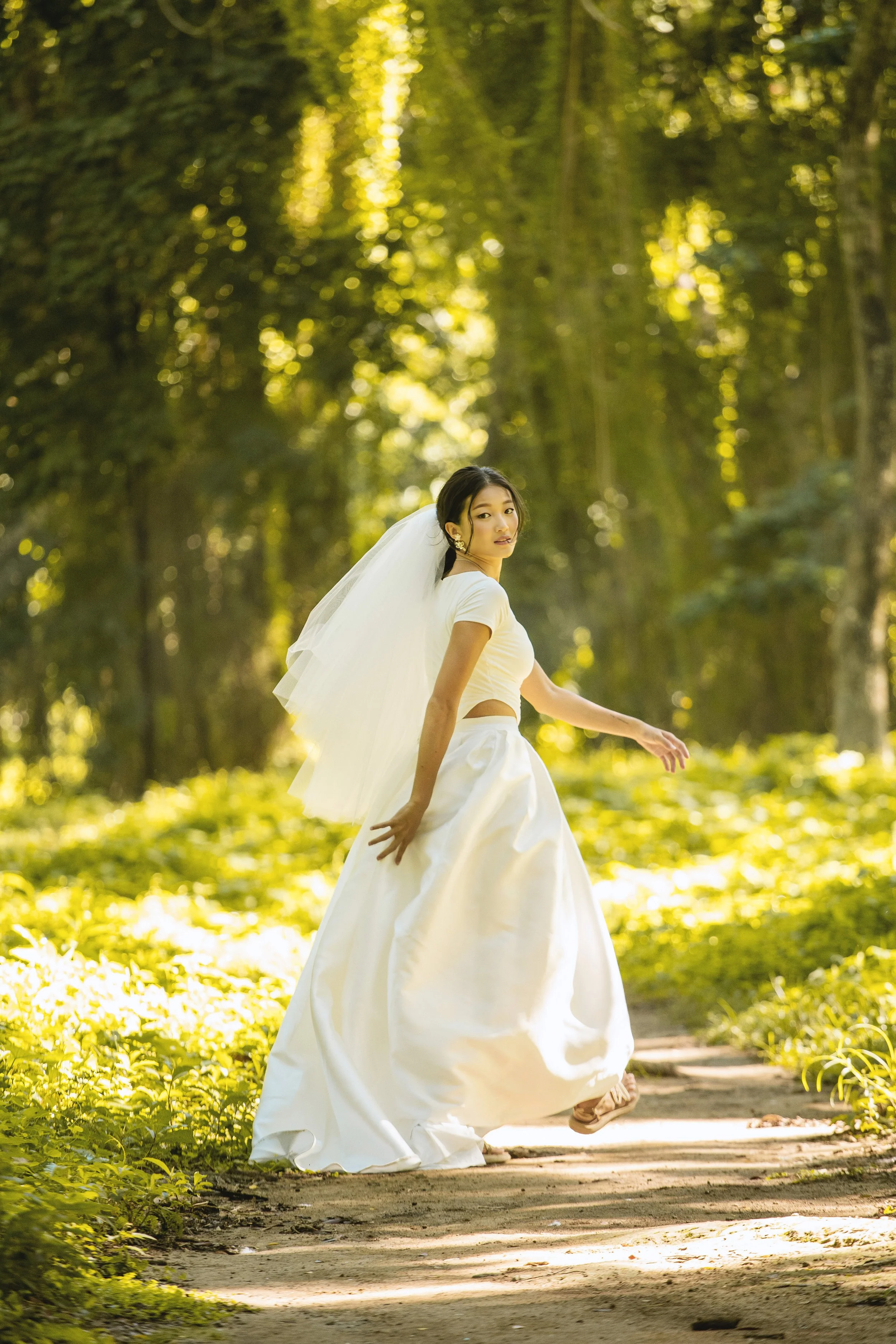 Bride in a white dress with a veil walking on a forest path