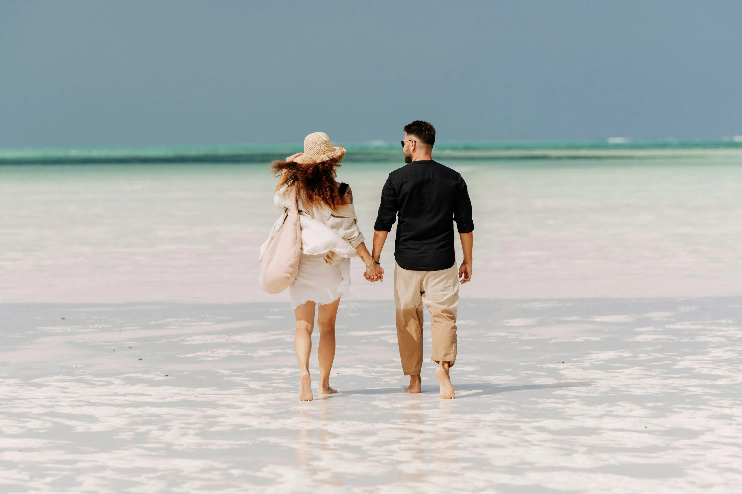 Person wearing a straw hat on a beach, facing the ocean.