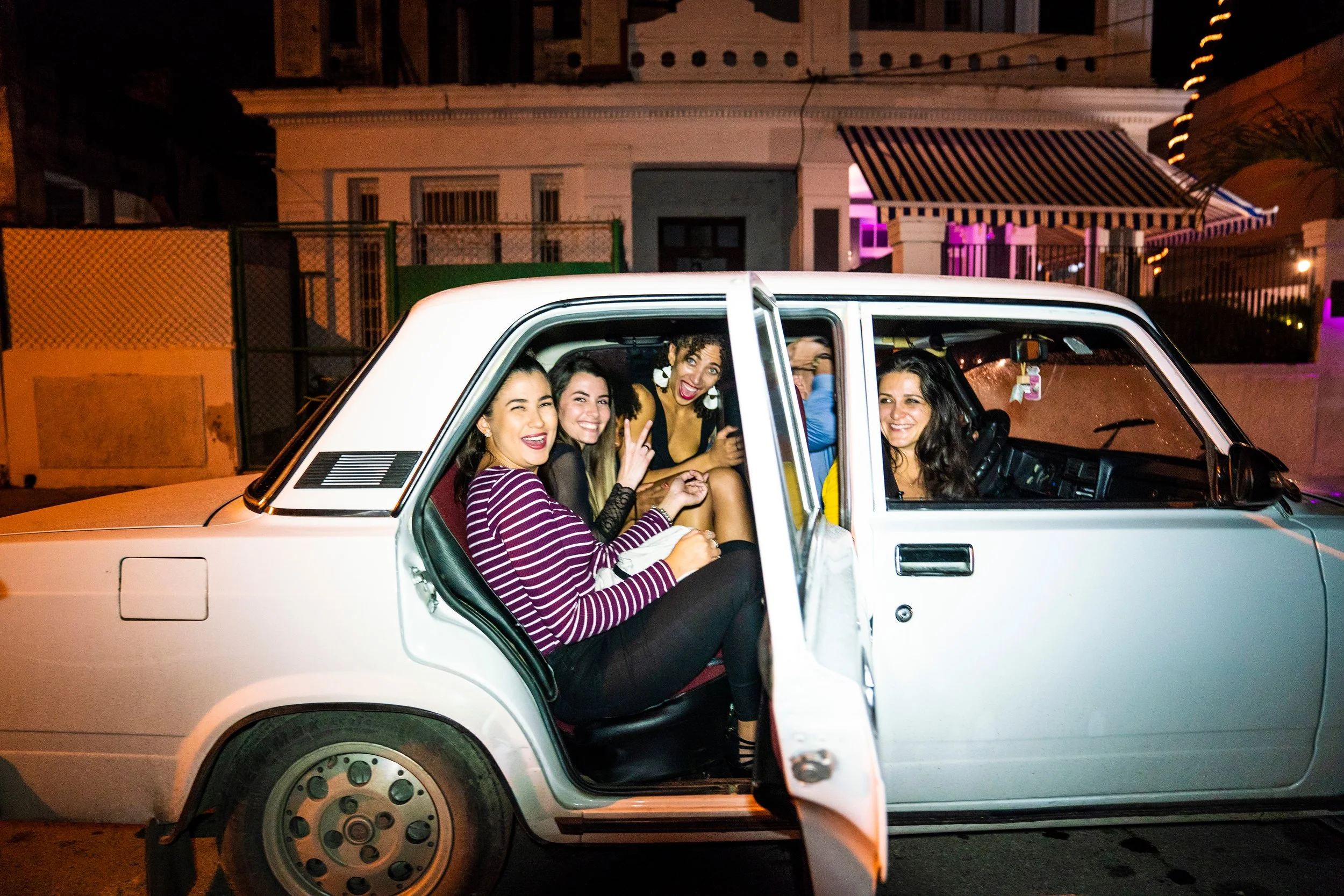 A smiling couple holding glasses with Havana Club logos in a bar with a neon 'Havana' sign in the background and a large sunflower in the foreground.