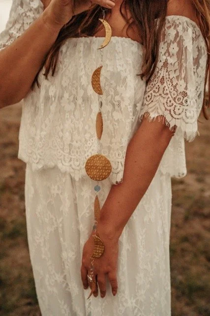 Een vrouw in een witte kanten jurk met een sierlijke hand en grote oorbellen die op de foto staan.