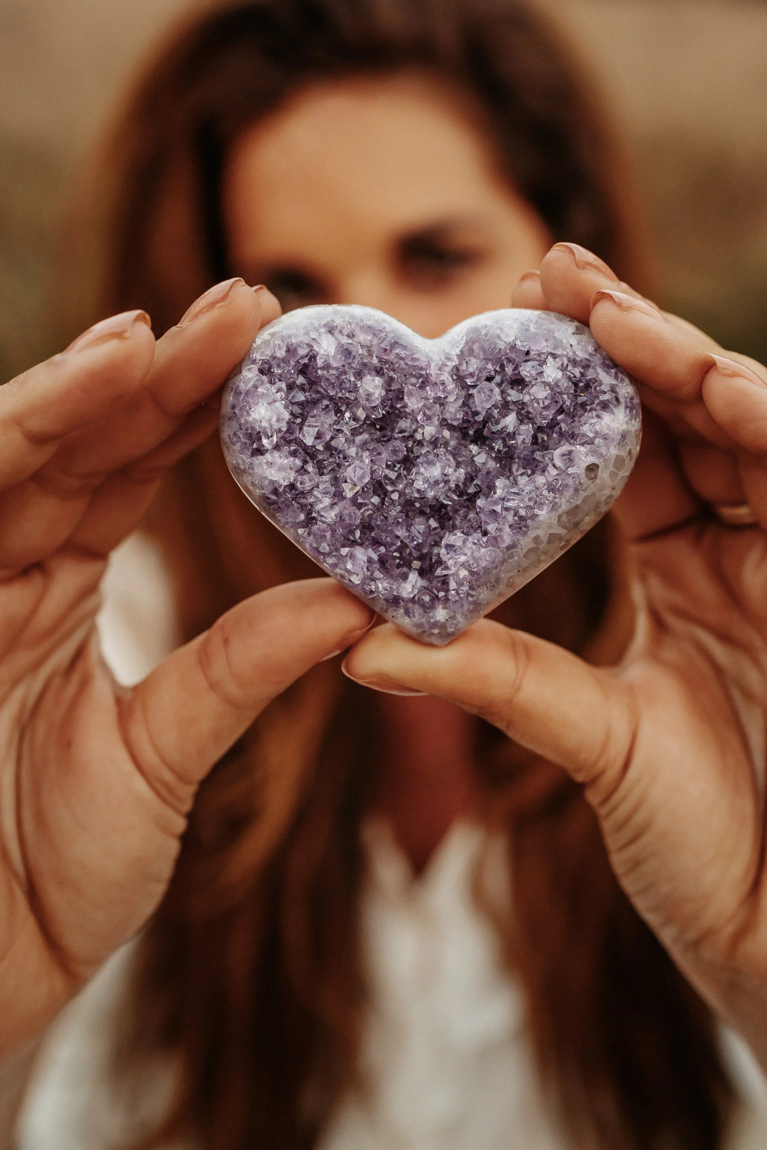Vrouw houdt een hartvormige kristal met paarse en doorzichtige kristallen, haar gezicht vaag op de achtergrond.