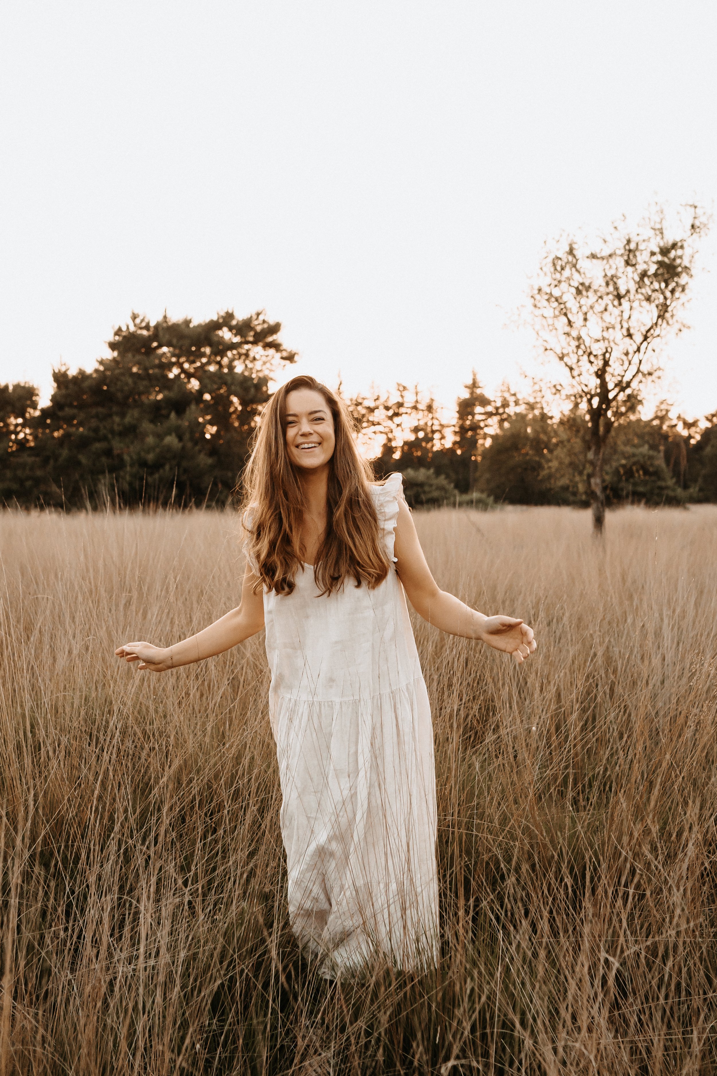 Vrouw in witte jurk in een veld met lange grassprieten tijdens zonsondergang