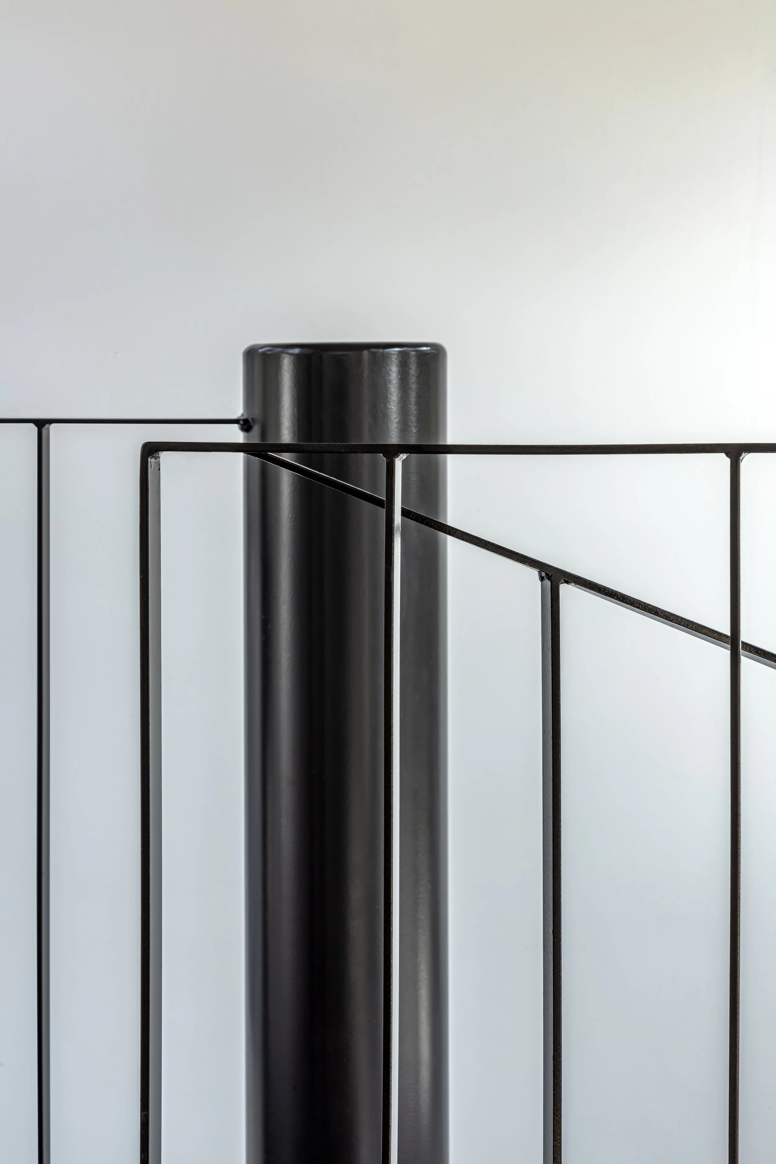 A black cylindrical object placed behind a black metal stand or grille against a plain white background.